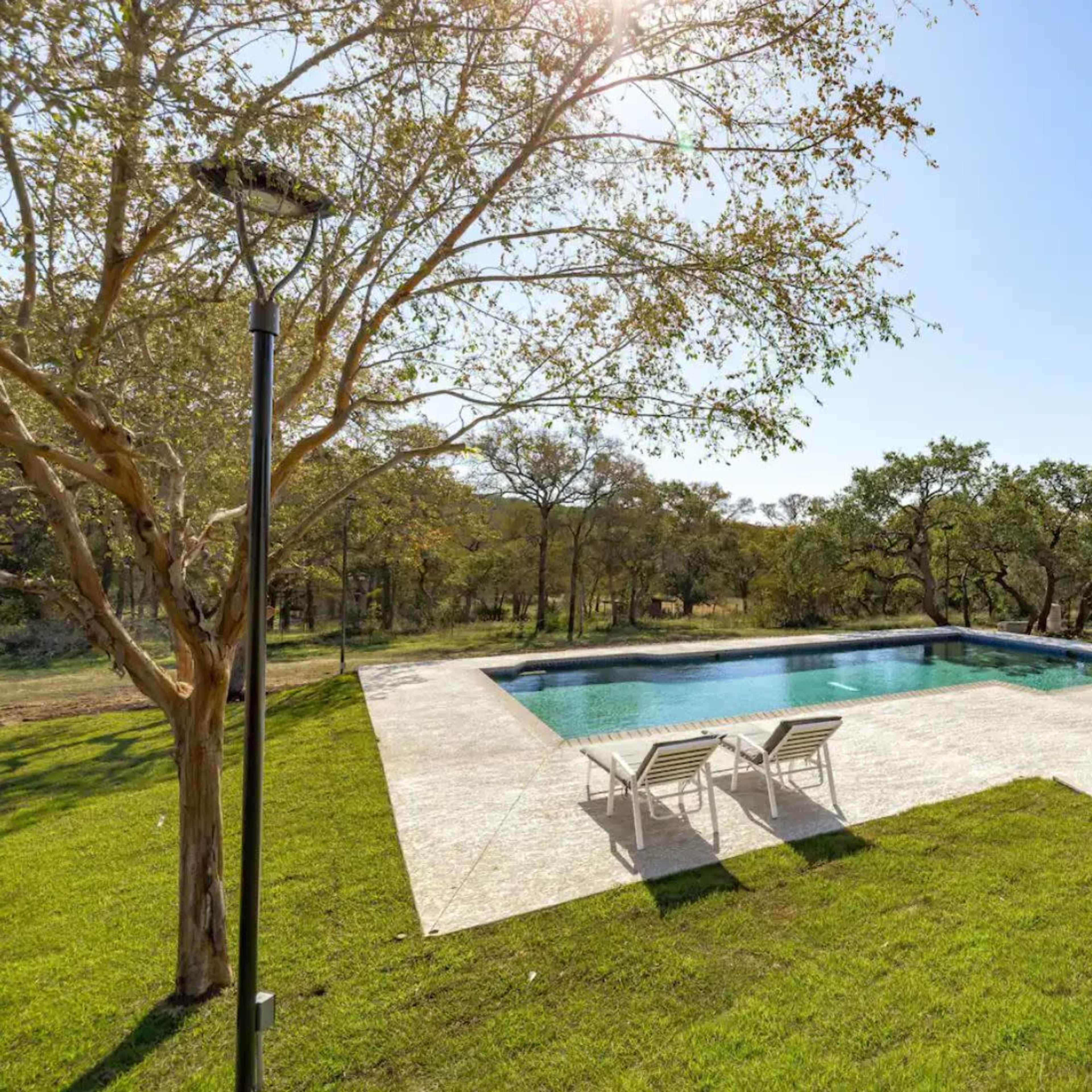A spacious outdoor area featuring a swimming pool surrounded by a lawn and trees.