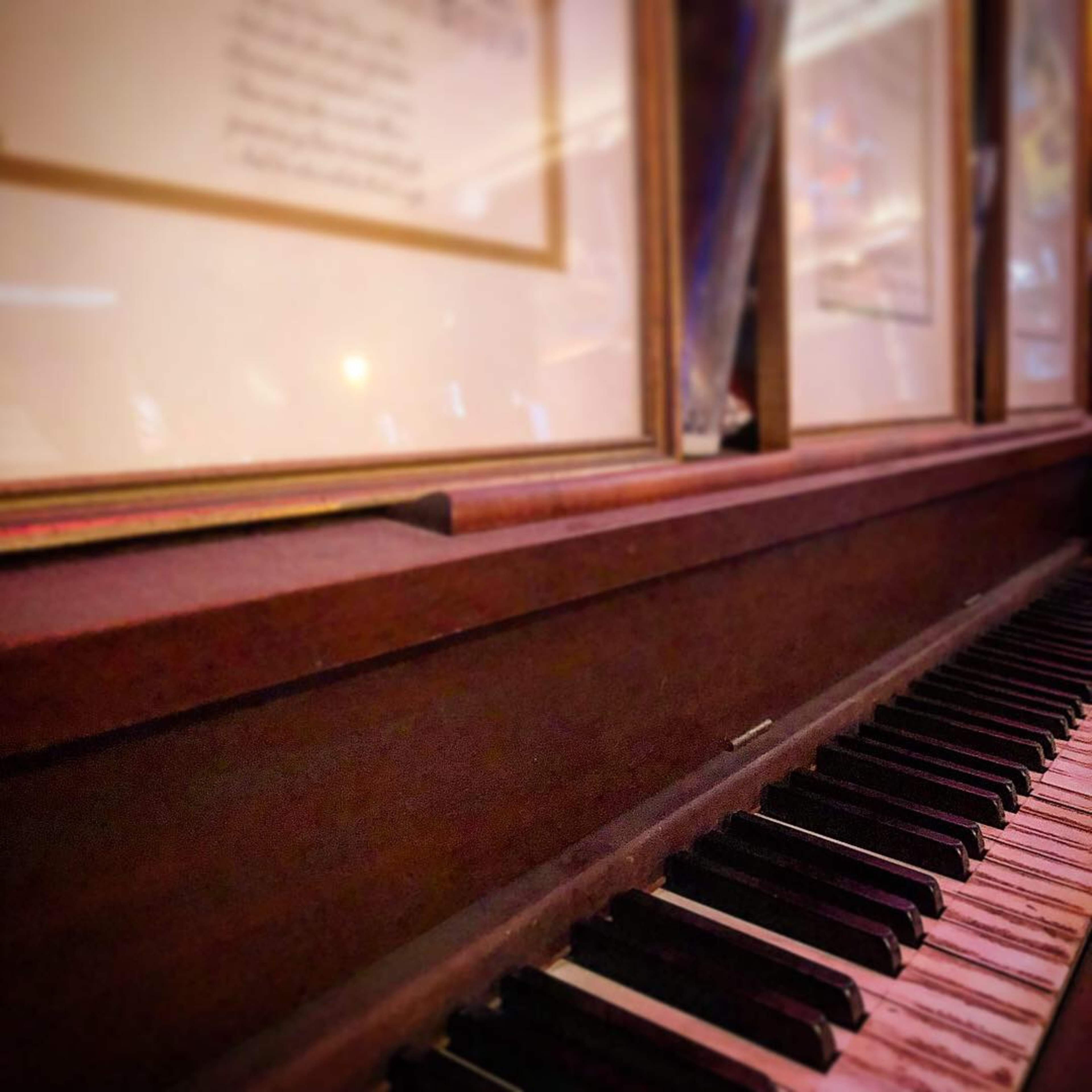 A close-up view of an old piano's keys with framed documents visible in the background.