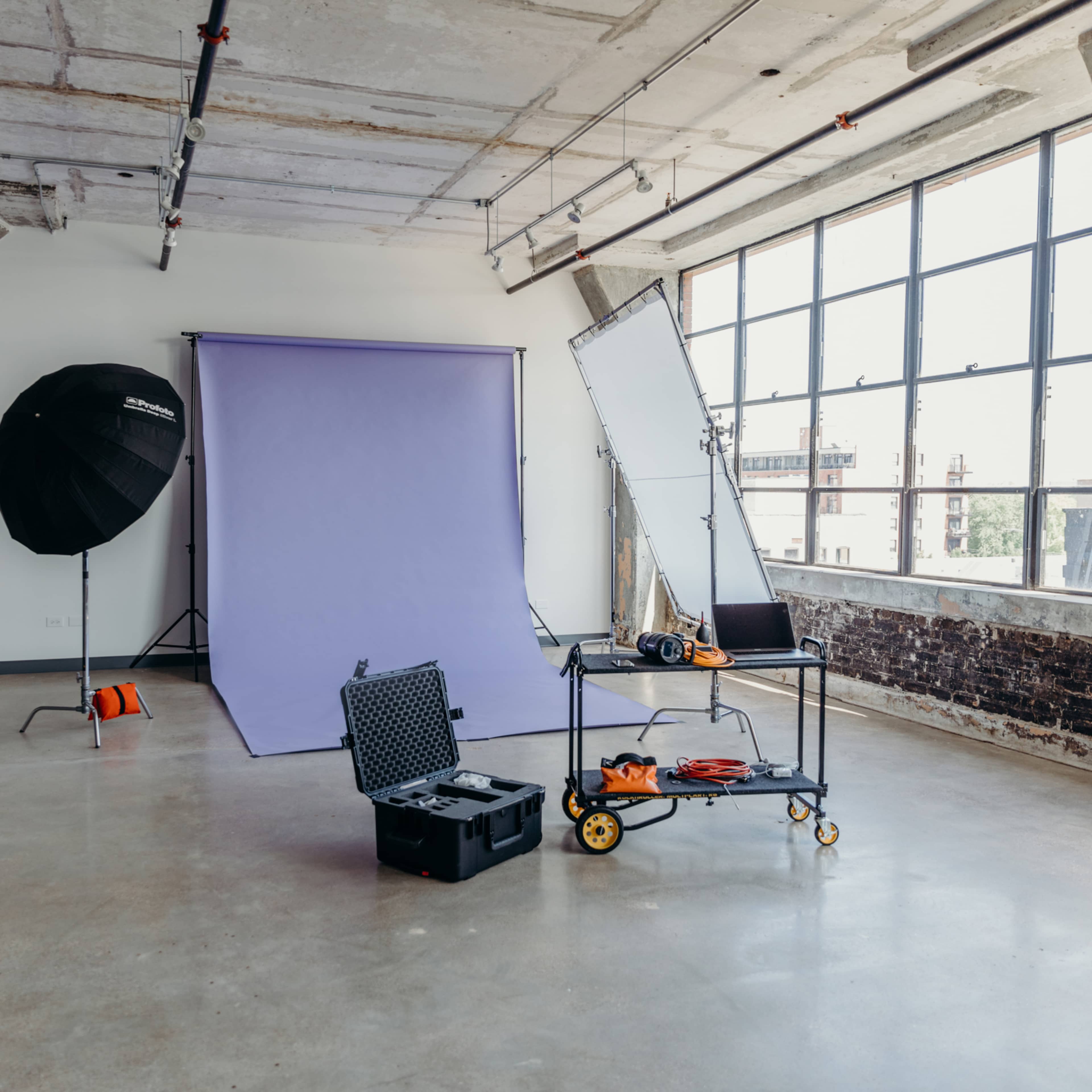 A photography studio with a purple backdrop, lighting equipment, and a cart with tools and accessories in an industrial-style space.
