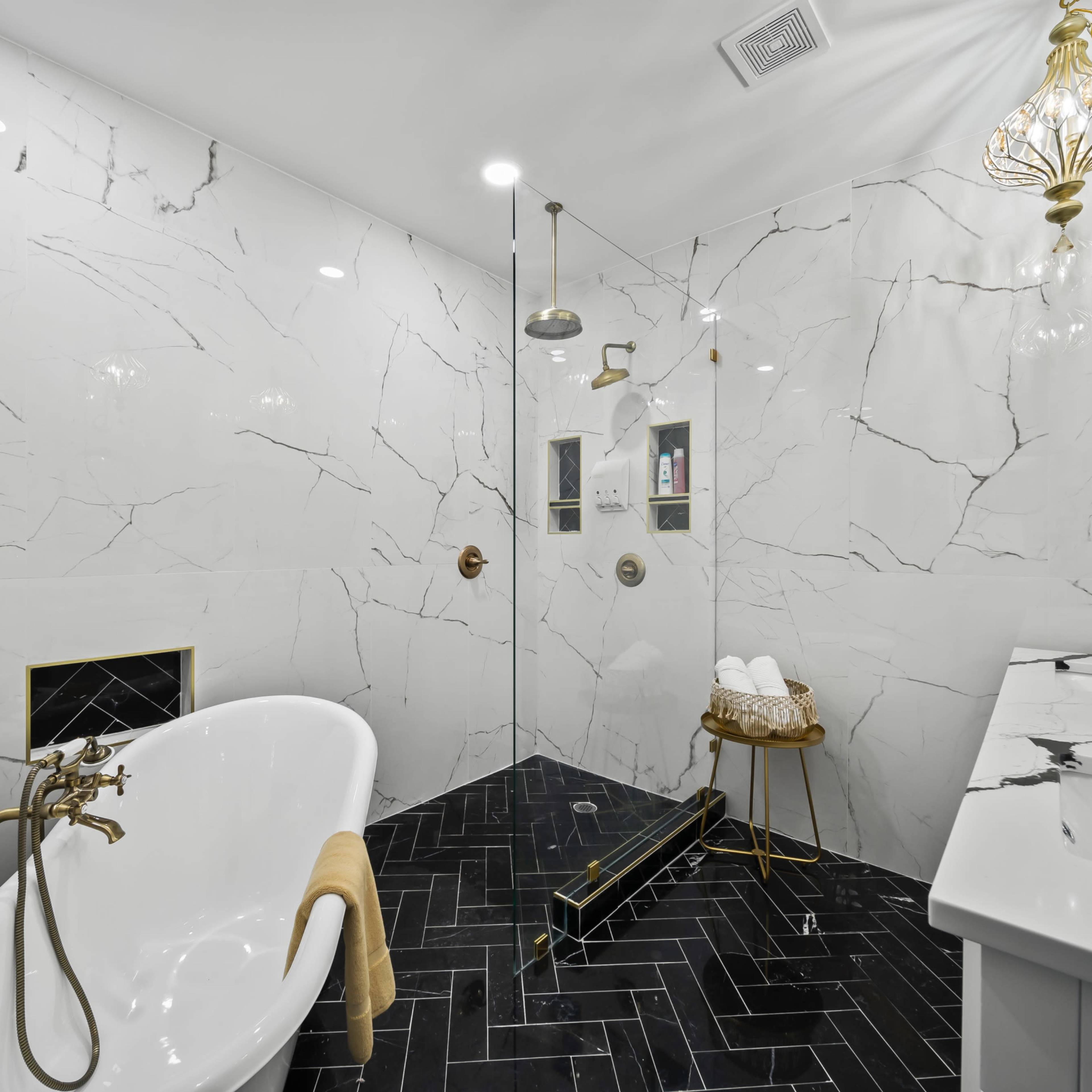 The bathroom features a freestanding bathtub, a glass shower with dual showerheads, and elegant black and white marble walls and flooring.