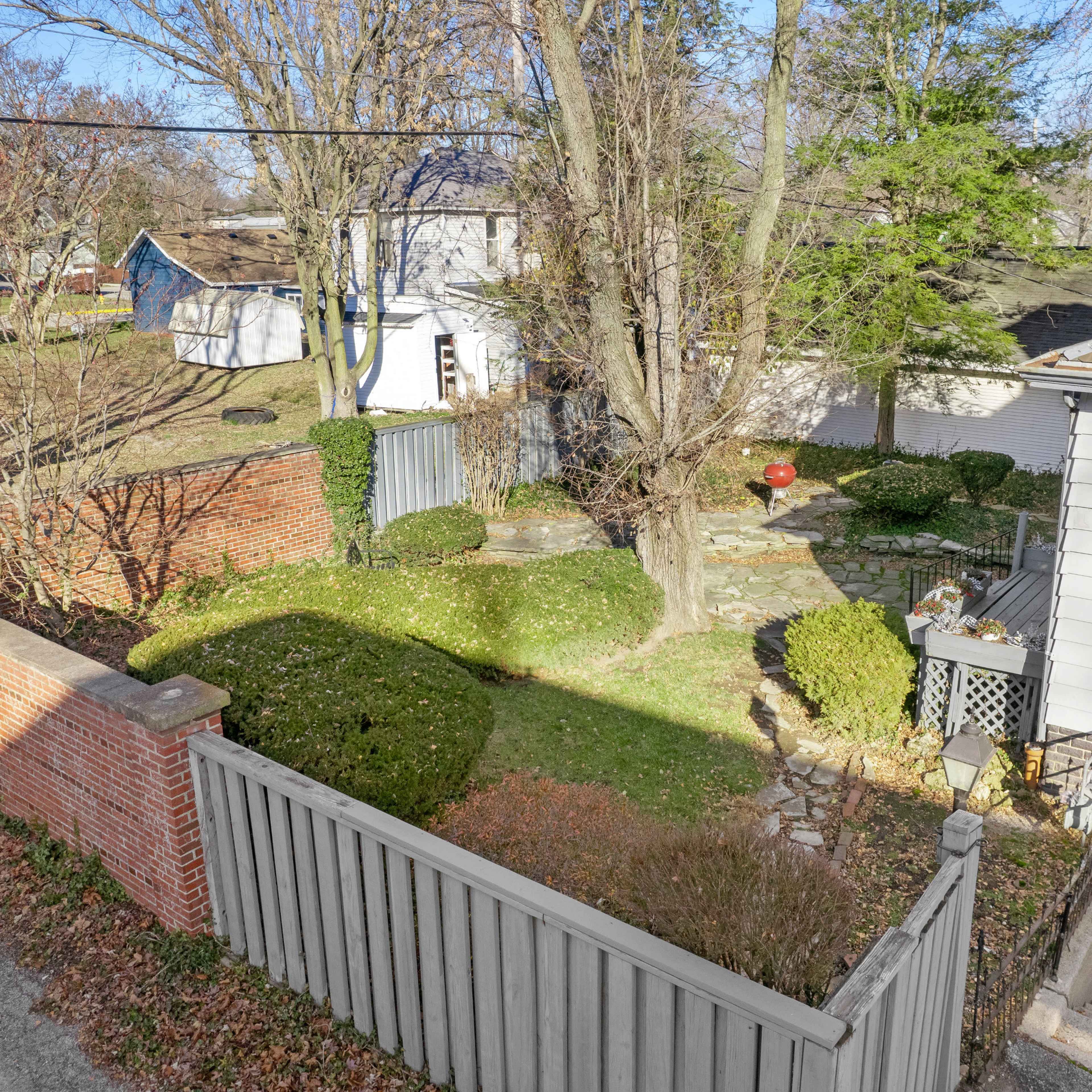 A residential backyard with a stone path, well-maintained shrubs, and a small wooden deck next to a house.