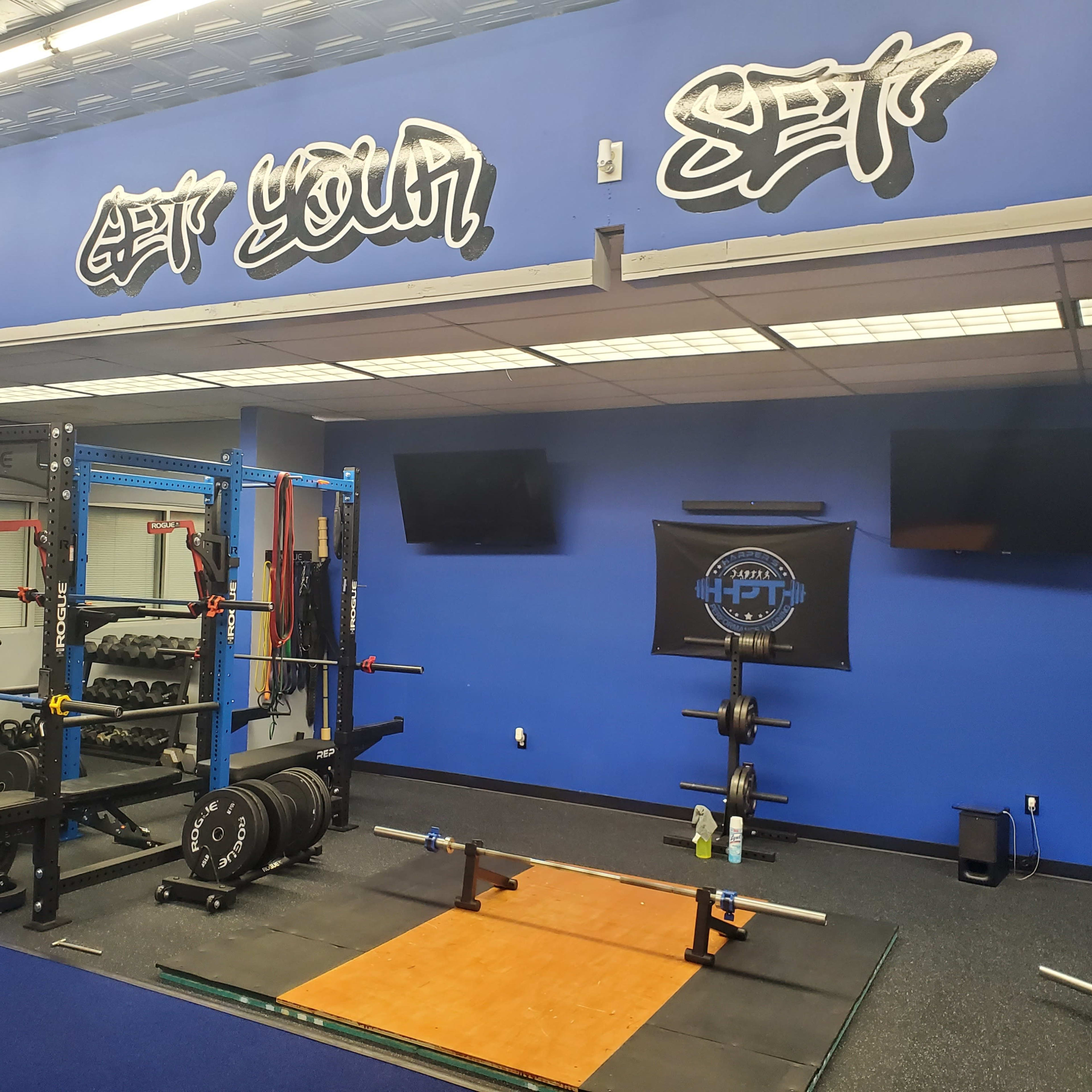 A fitness gym interior with weightlifting equipment, including a squat rack, free weights, and a weightlifting platform.
