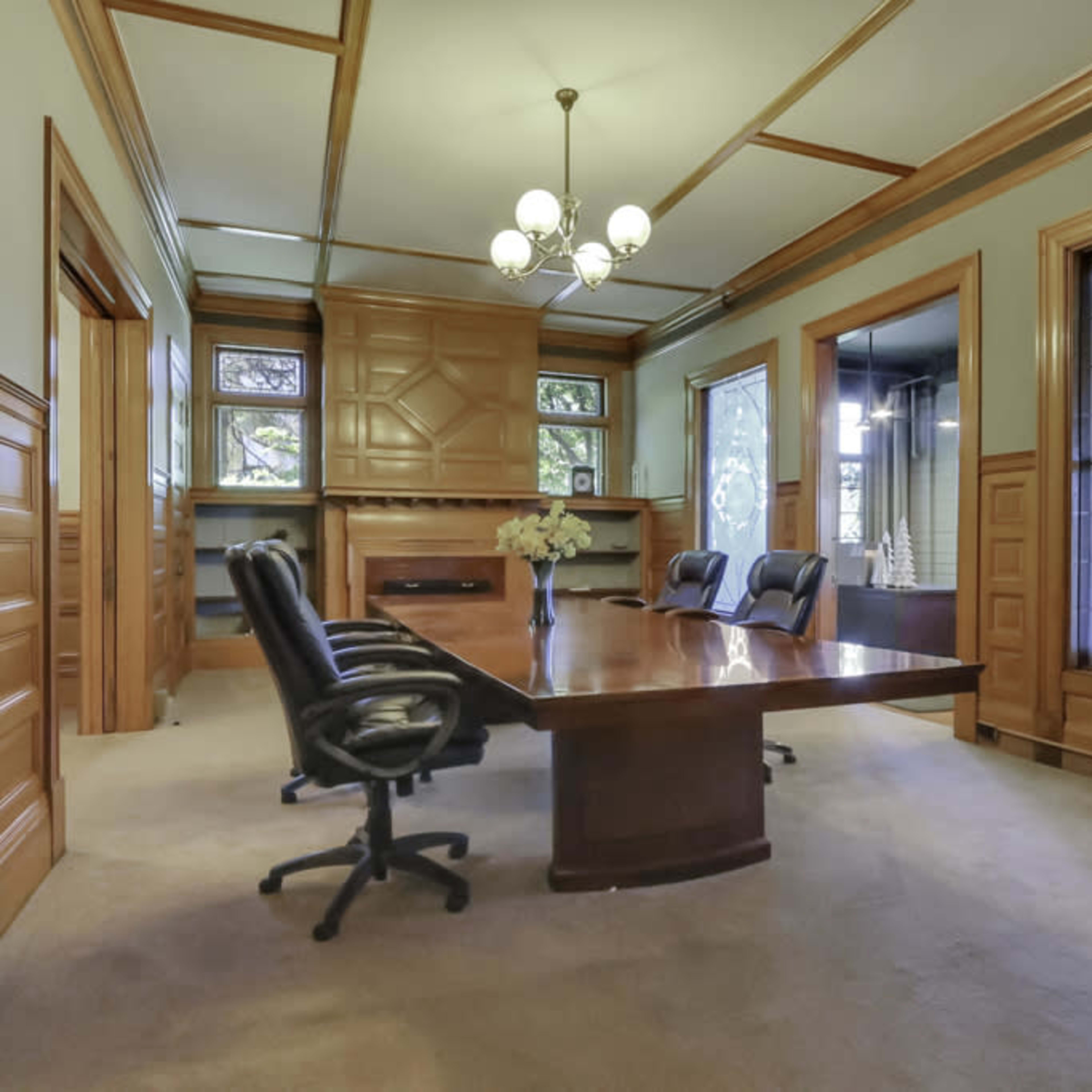 A wooden conference room with a large table and several office chairs, featuring ornate paneling and decorative windows.