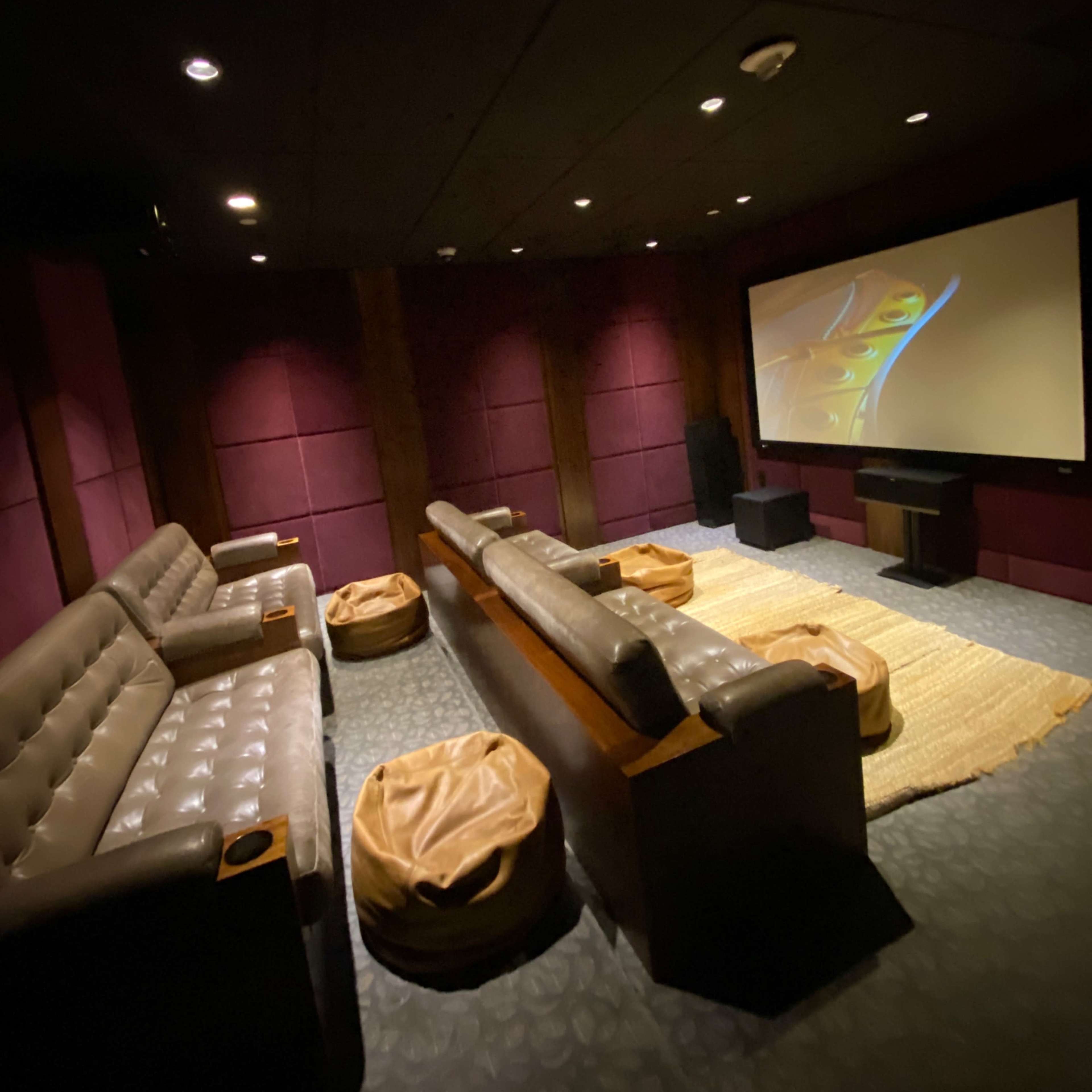 A dimly lit home theater with leather seating, bean bag chairs, and a large screen at the front.
