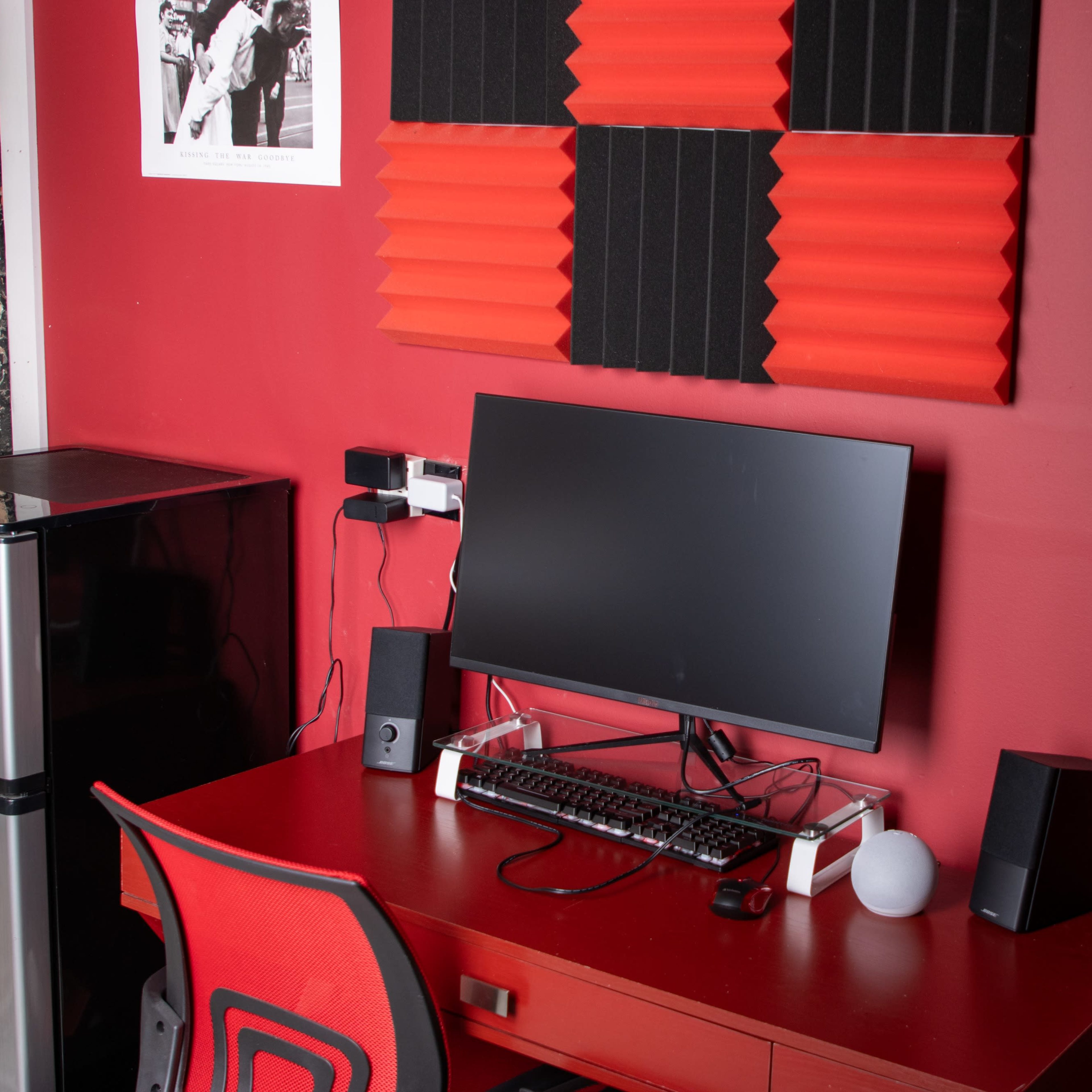 A home office setup with a computer monitor on a red desk, surrounded by red and black sound-absorbing panels on the wall.