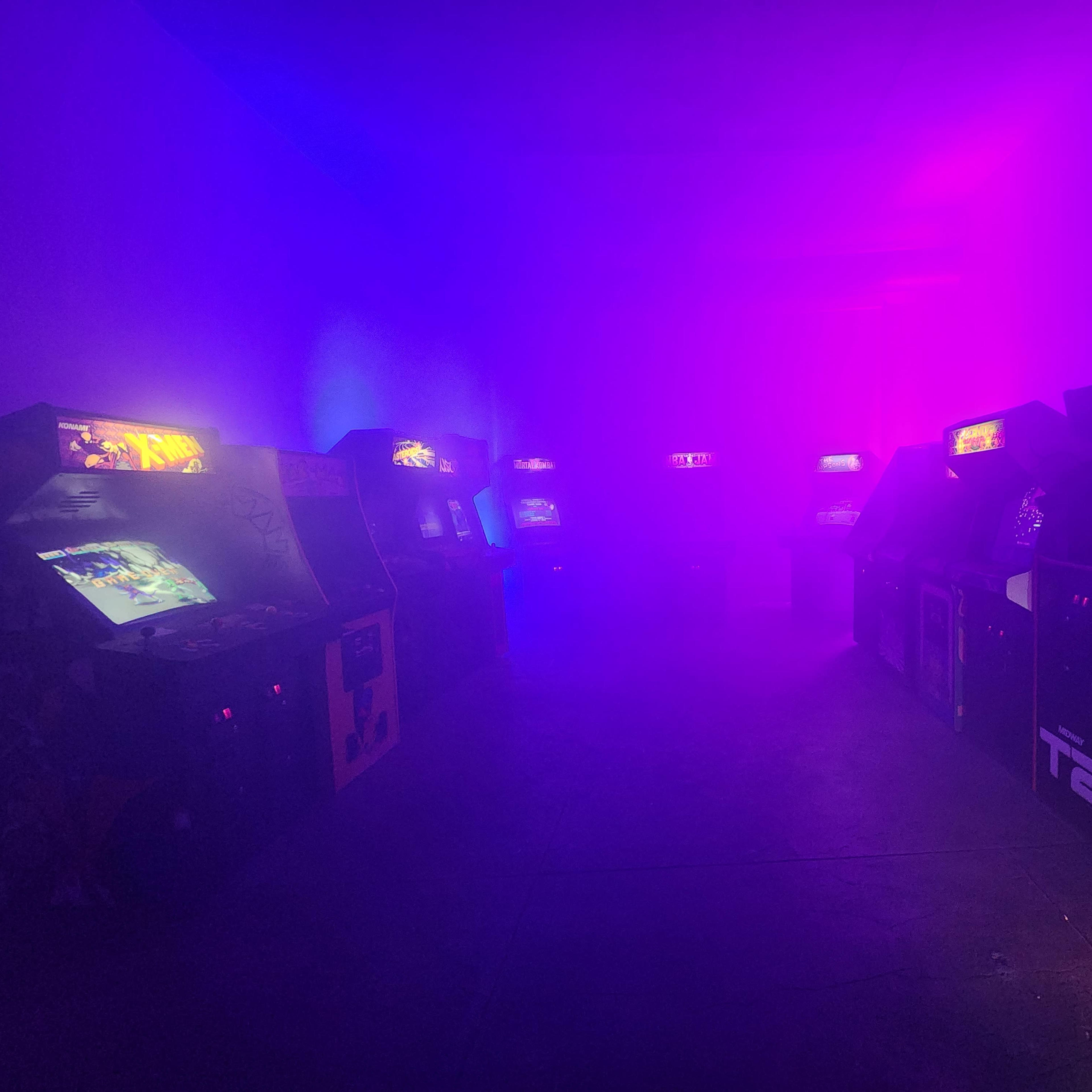 The scene features a dimly lit arcade room filled with several vintage arcade machines, shrouded in purple and blue fog.