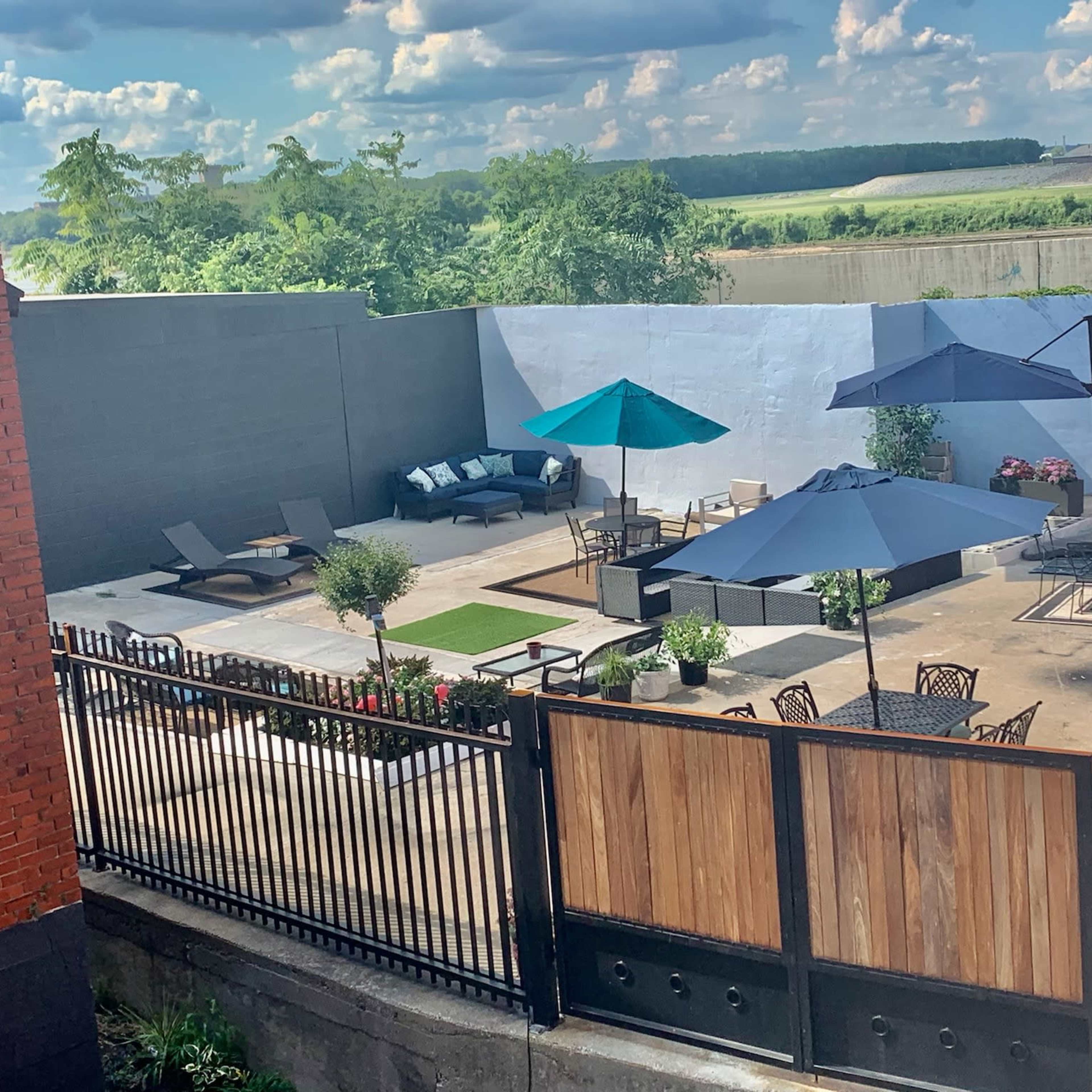 A large outdoor patio area with seating, umbrellas, and planters, surrounded by a gray wall.