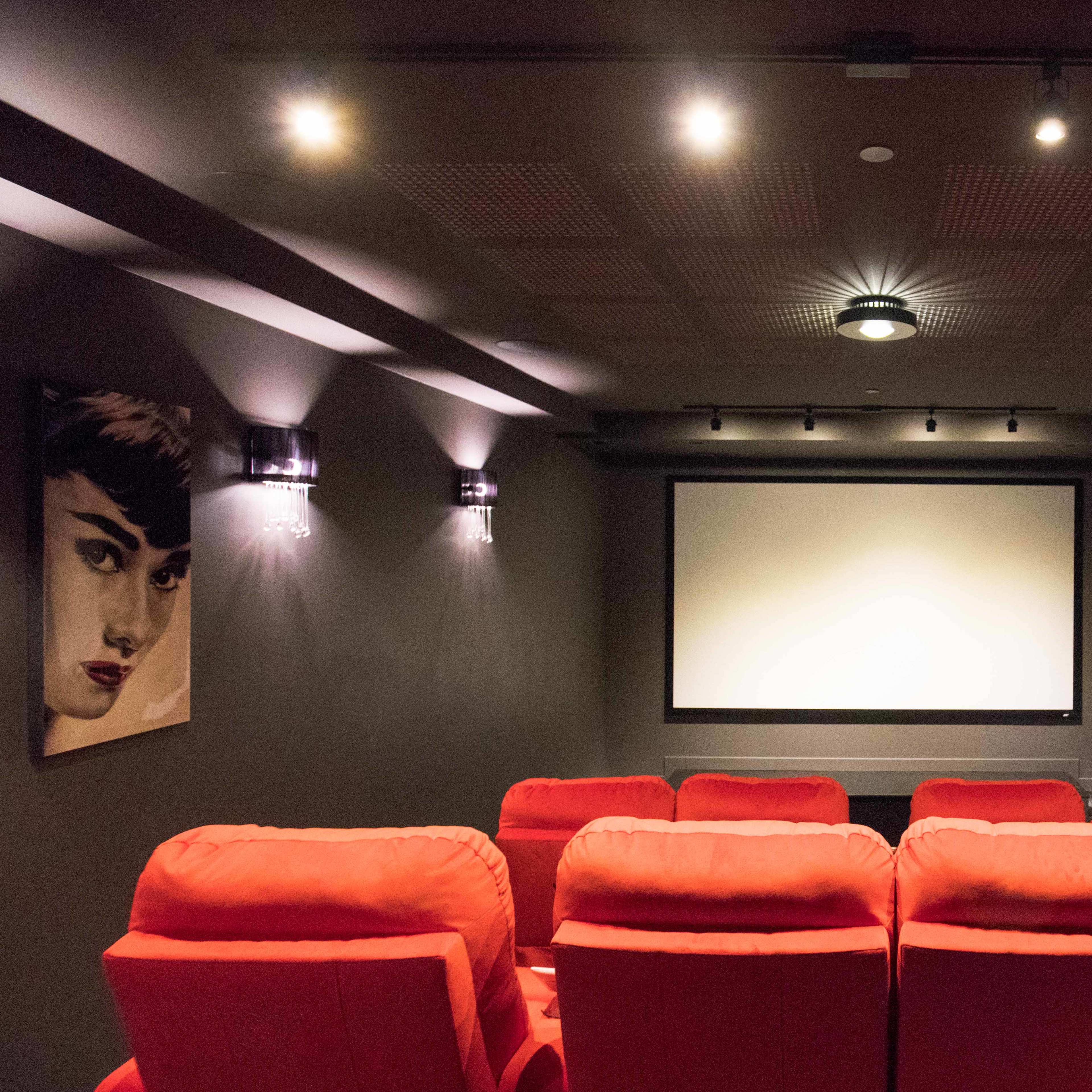 A home theater with red recliner seats facing a large white screen, flanked by black and white portraits of iconic actresses on the walls.