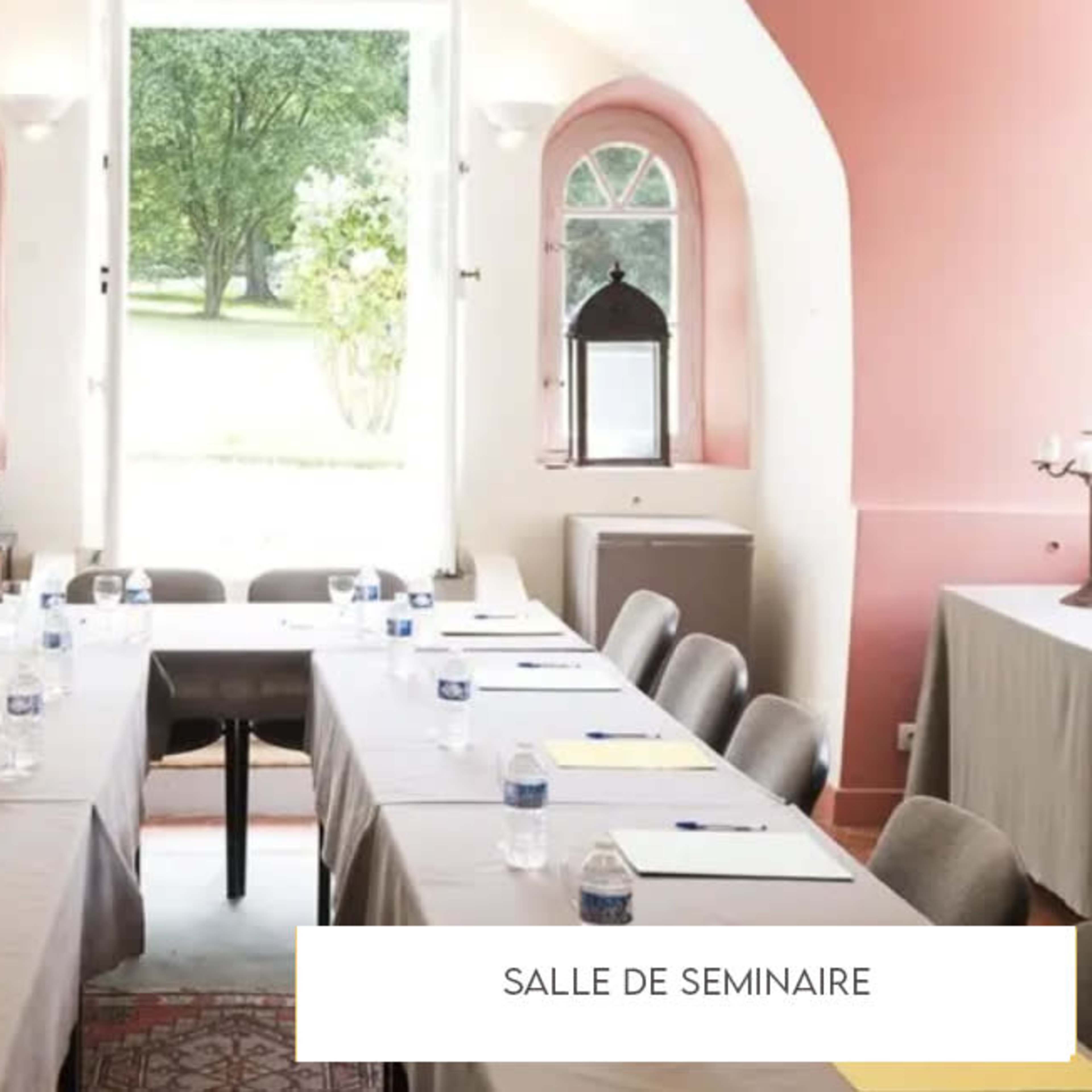 A seminar room is set up with a long table covered in gray cloth, featuring chairs, water bottles, and yellow notepads, while open doors lead to a view of greenery outside.