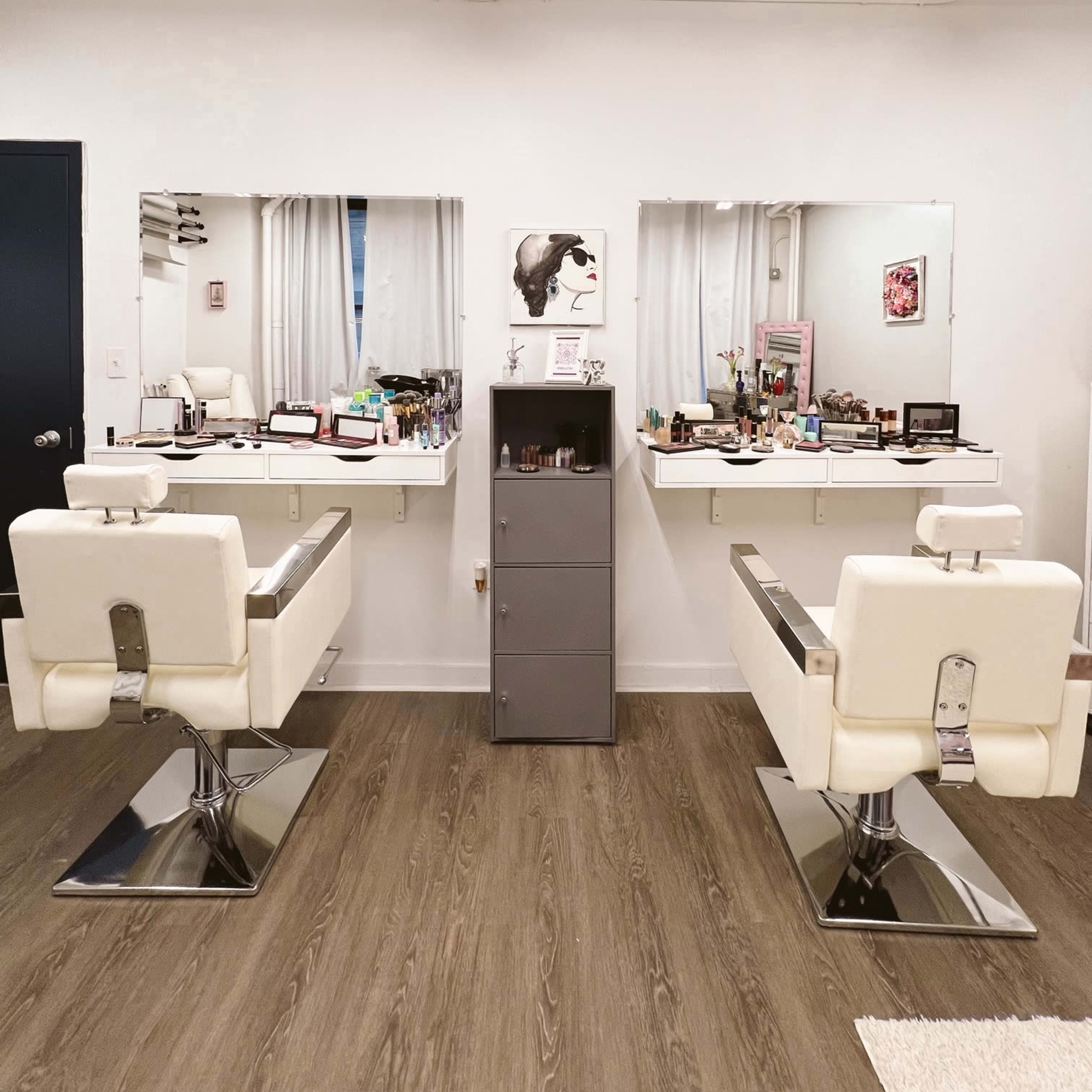 A modern hair salon with two white styling chairs, large mirrors above each station, and a gray storage cabinet in the center.