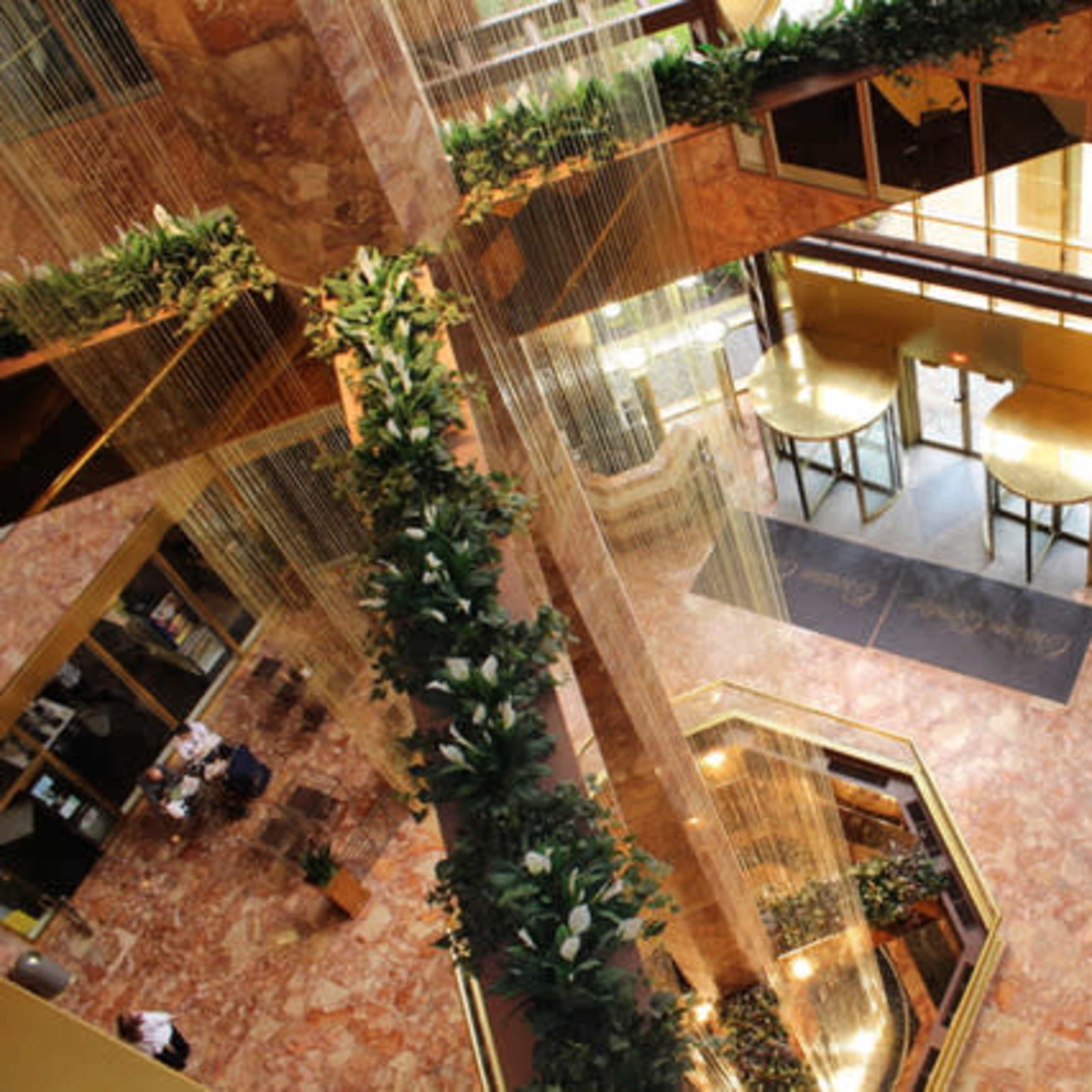 The interior of a multi-level atrium with marble flooring, greenery, and a seating area near large glass doors.