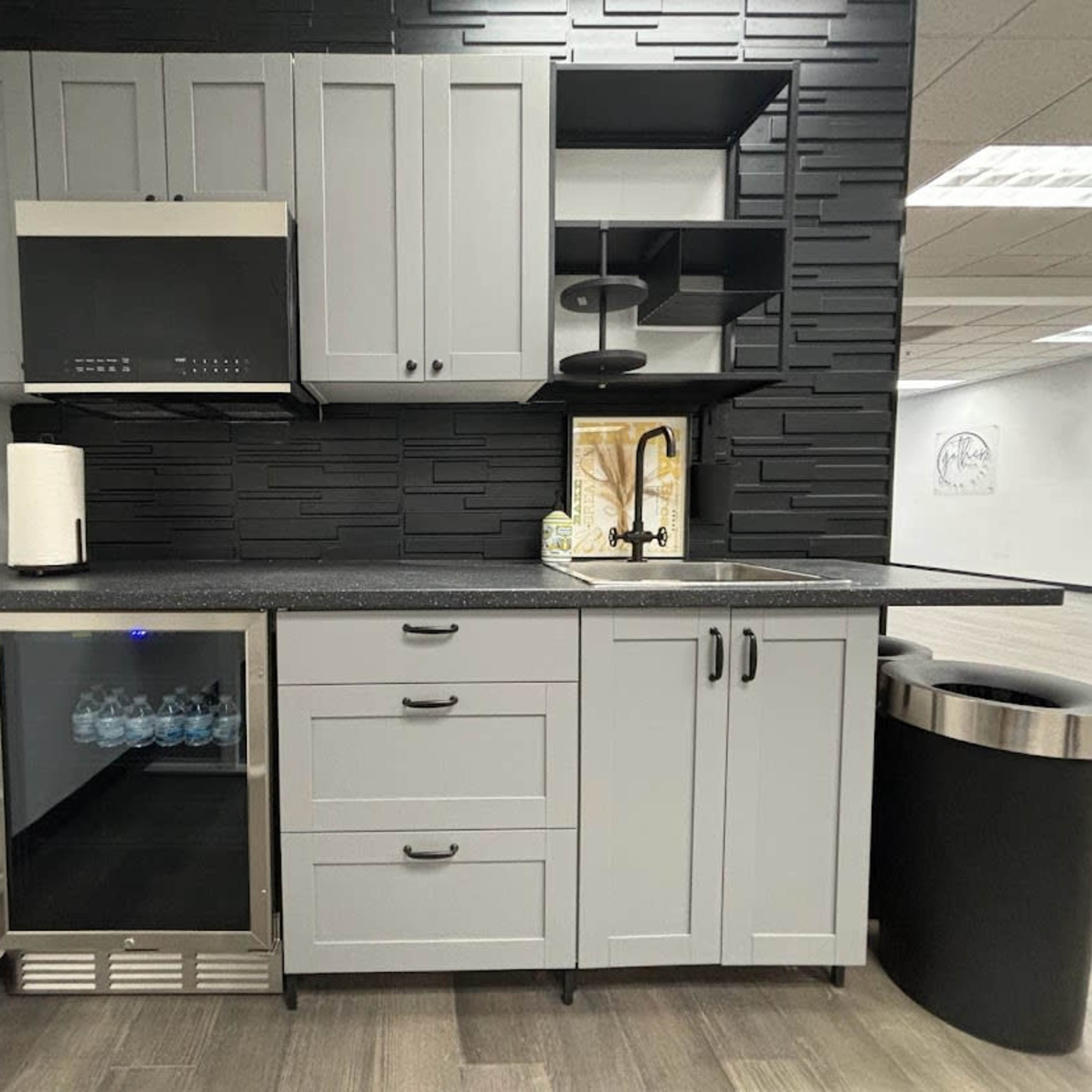 A modern kitchen arrangement featuring gray cabinets, a stainless steel refrigerator, a sink, and a black shelving unit against a textured wall.