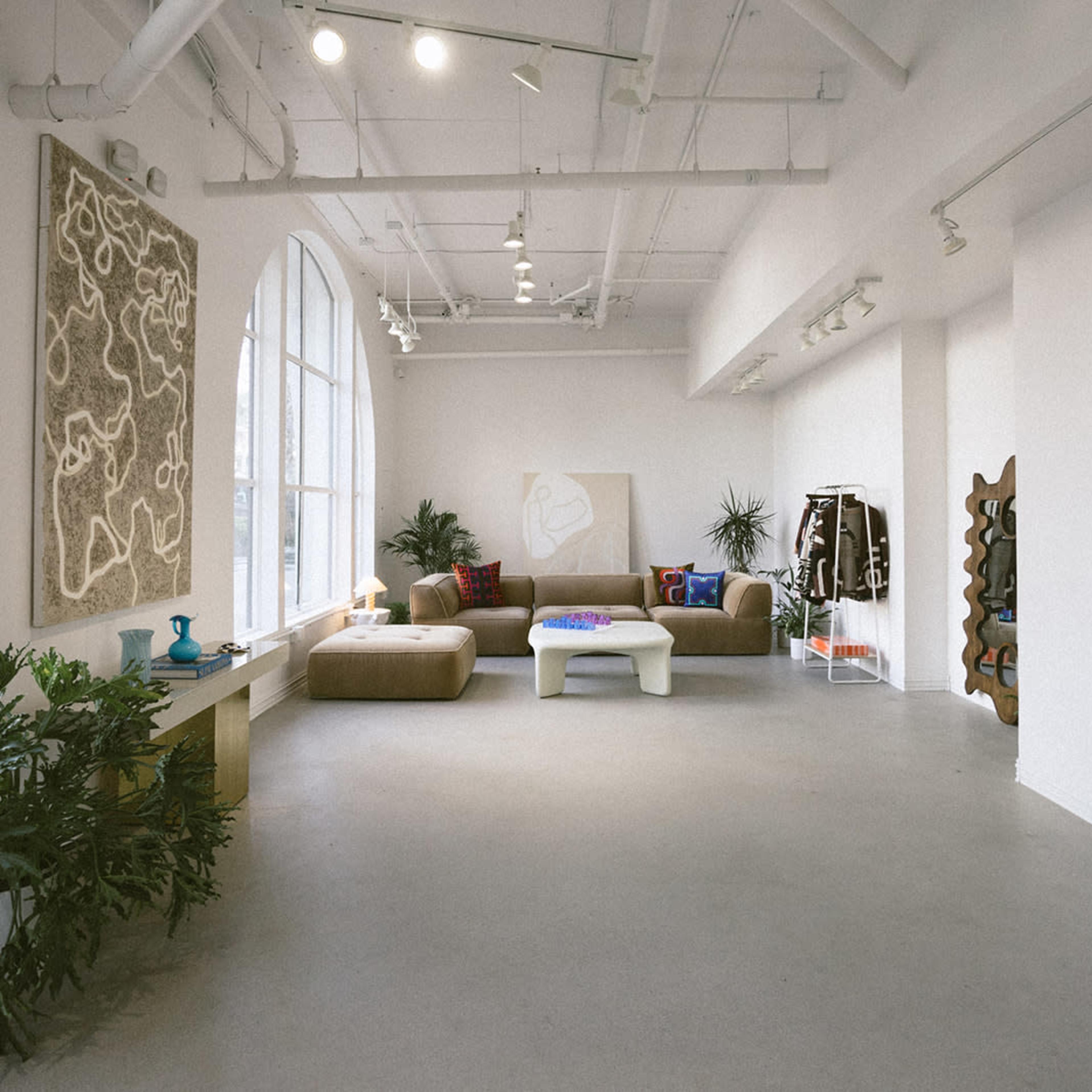 A spacious, minimalist gallery-like room features a large window, a brown sofa, a coffee table, and modern art on the walls.