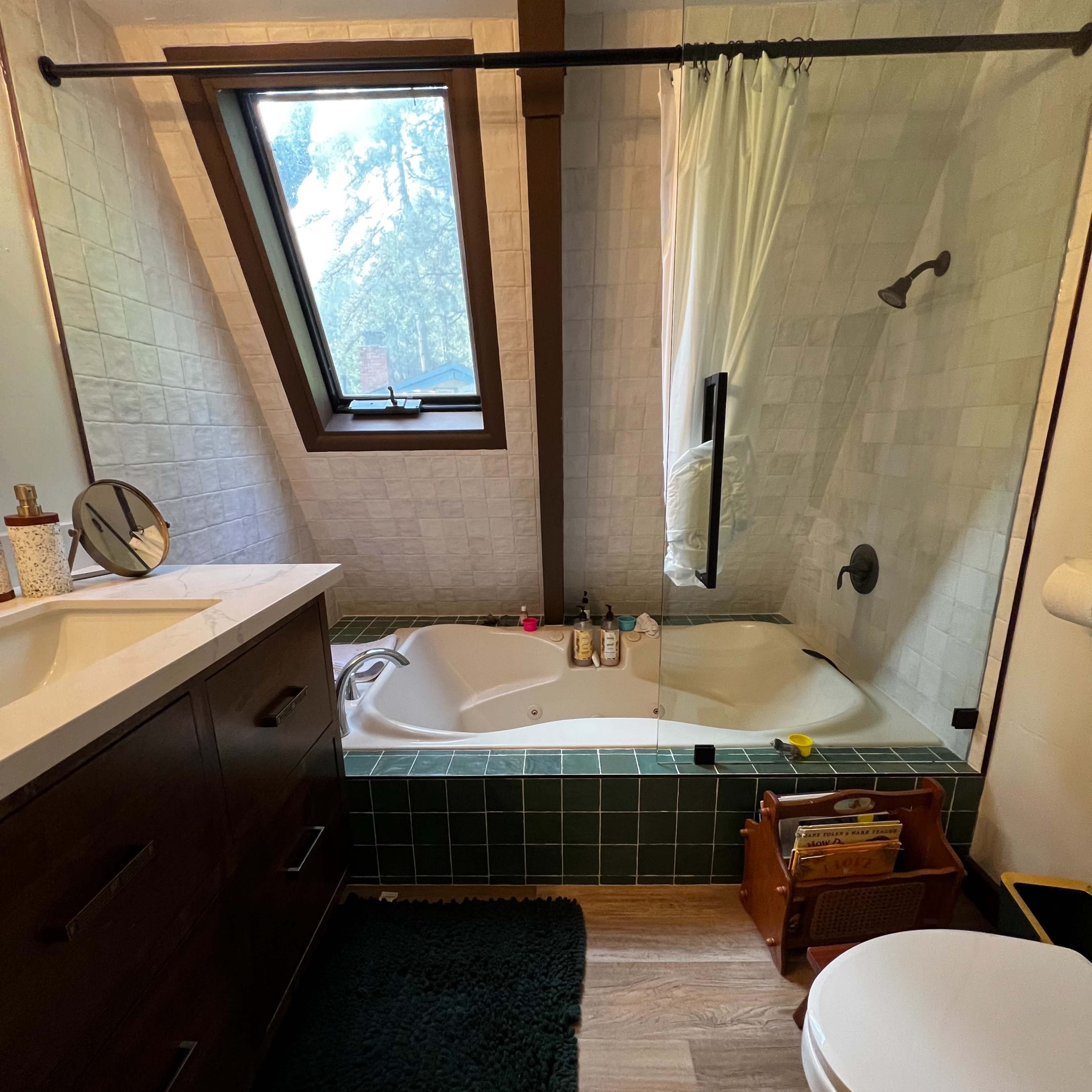 A modern bathroom featuring a bathtub with a shower, a vanity with a mirror, and a toilet, all set under an angled window.