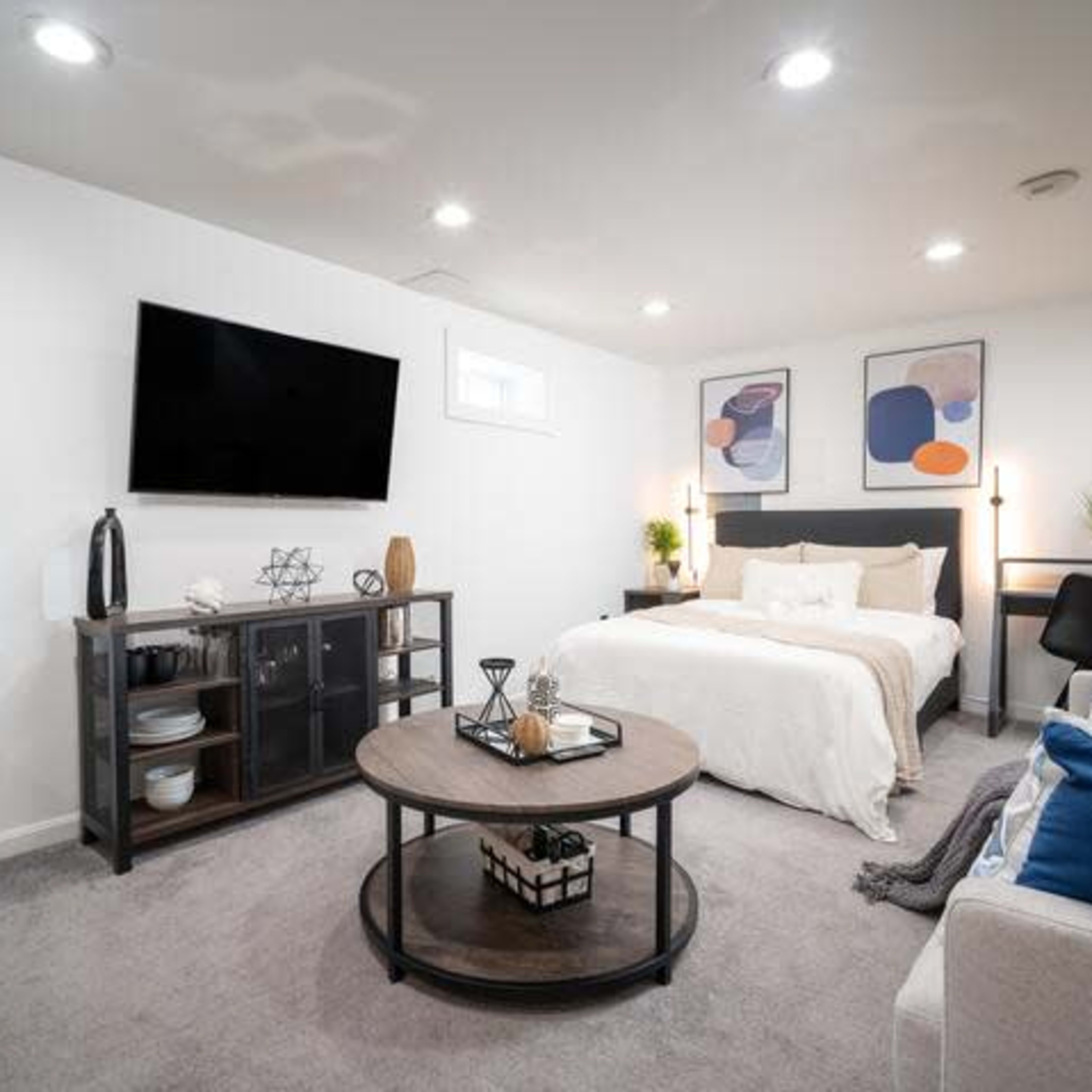 A modern studio apartment features a bed against a wall, a television mounted above, and a seating area with a coffee table and decorative elements.