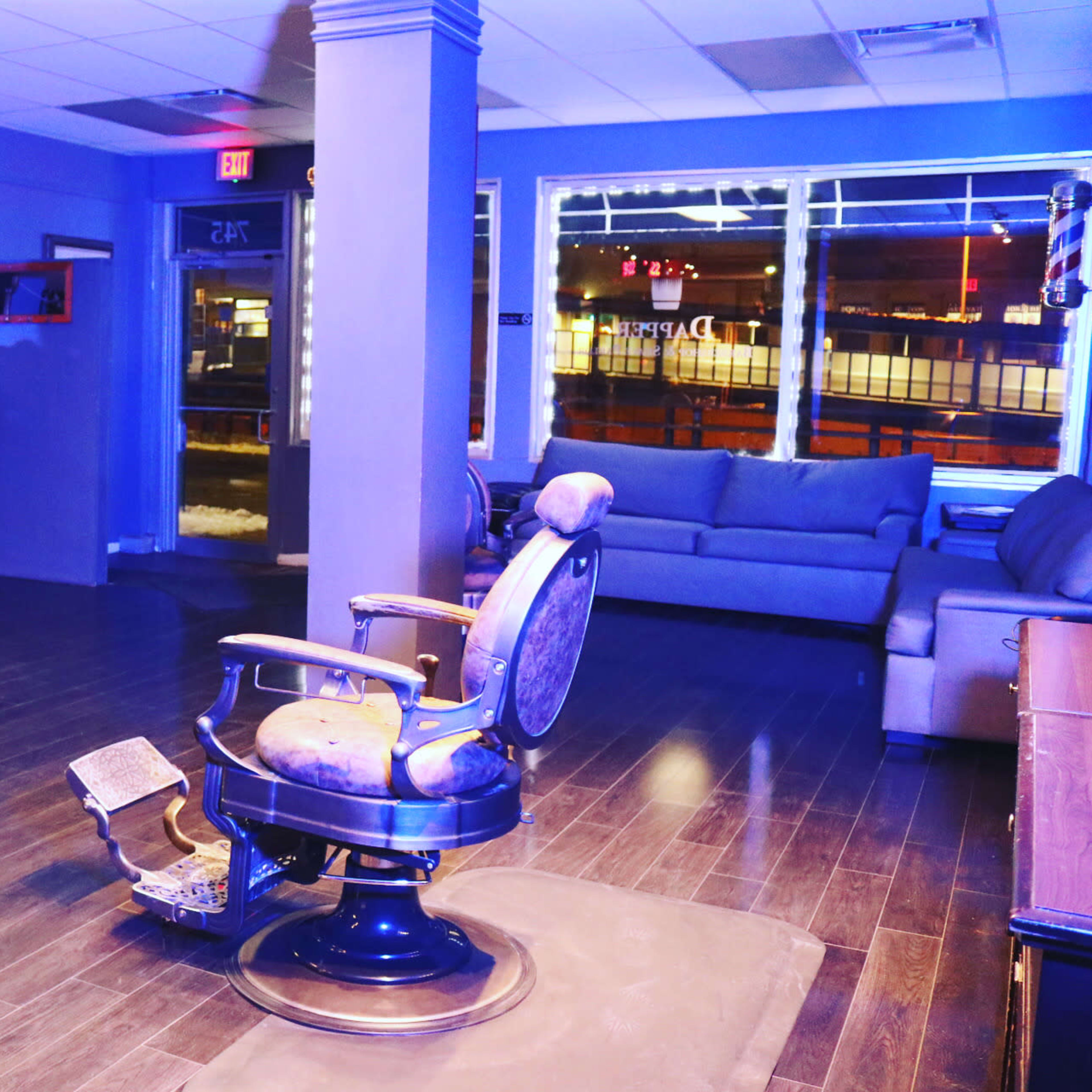 A modern barbershop interior featuring two barber chairs, a large screen displaying Netflix, and a seating area with a couch.