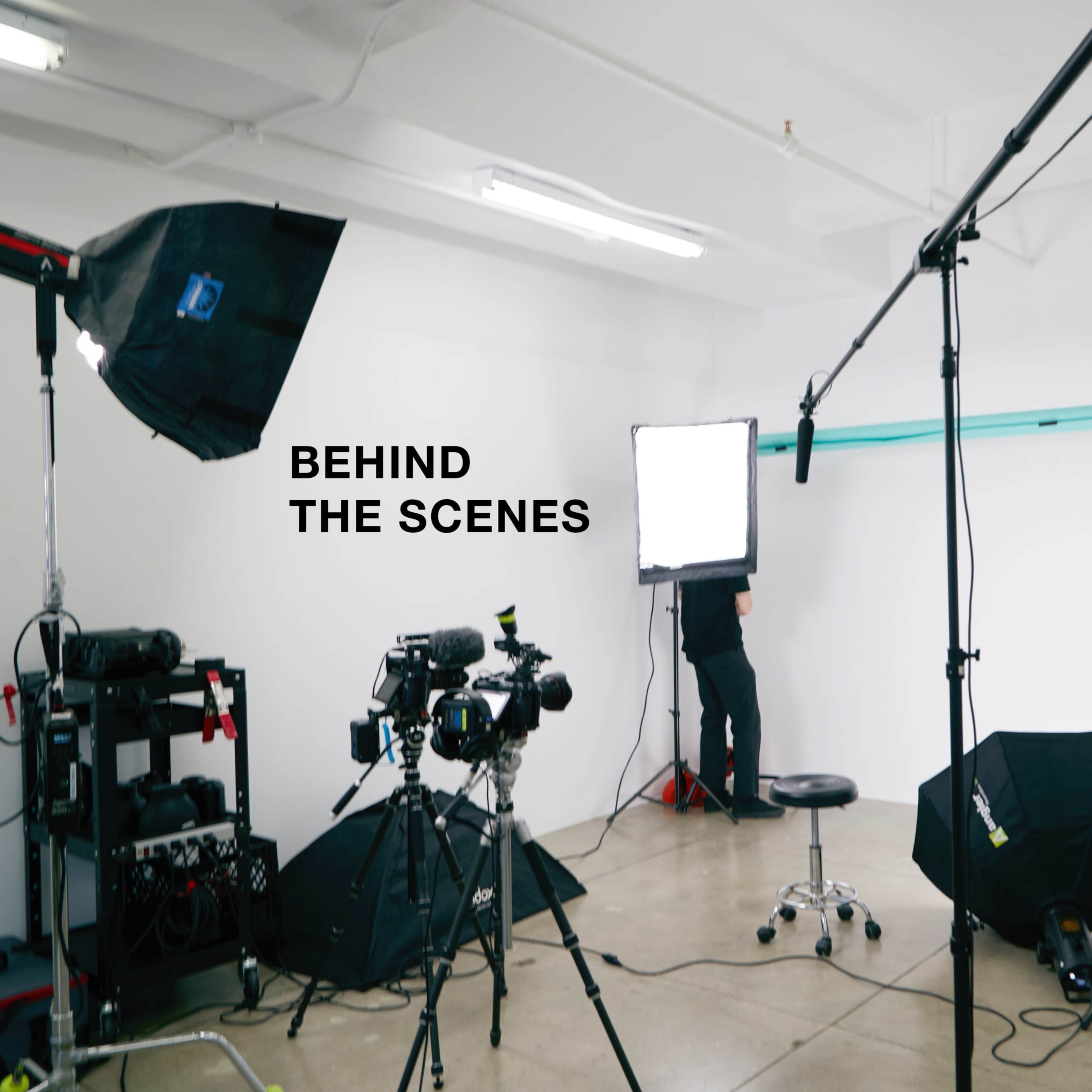 A photography studio setup with various lights, cameras, and equipment, including a backdrop and a person adjusting a light.