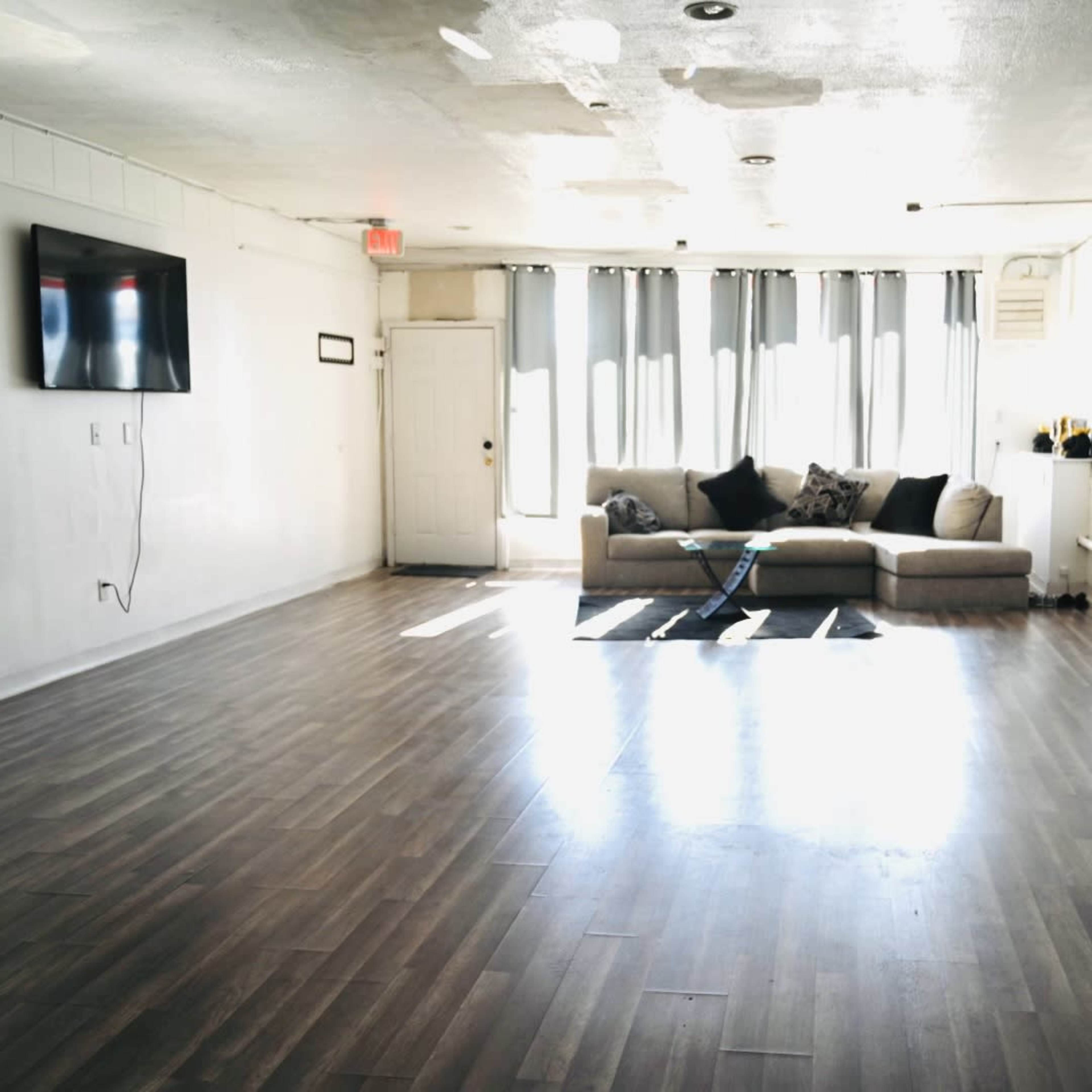 A spacious, empty room with a gray couch against the wall and a television mounted on the opposite wall.