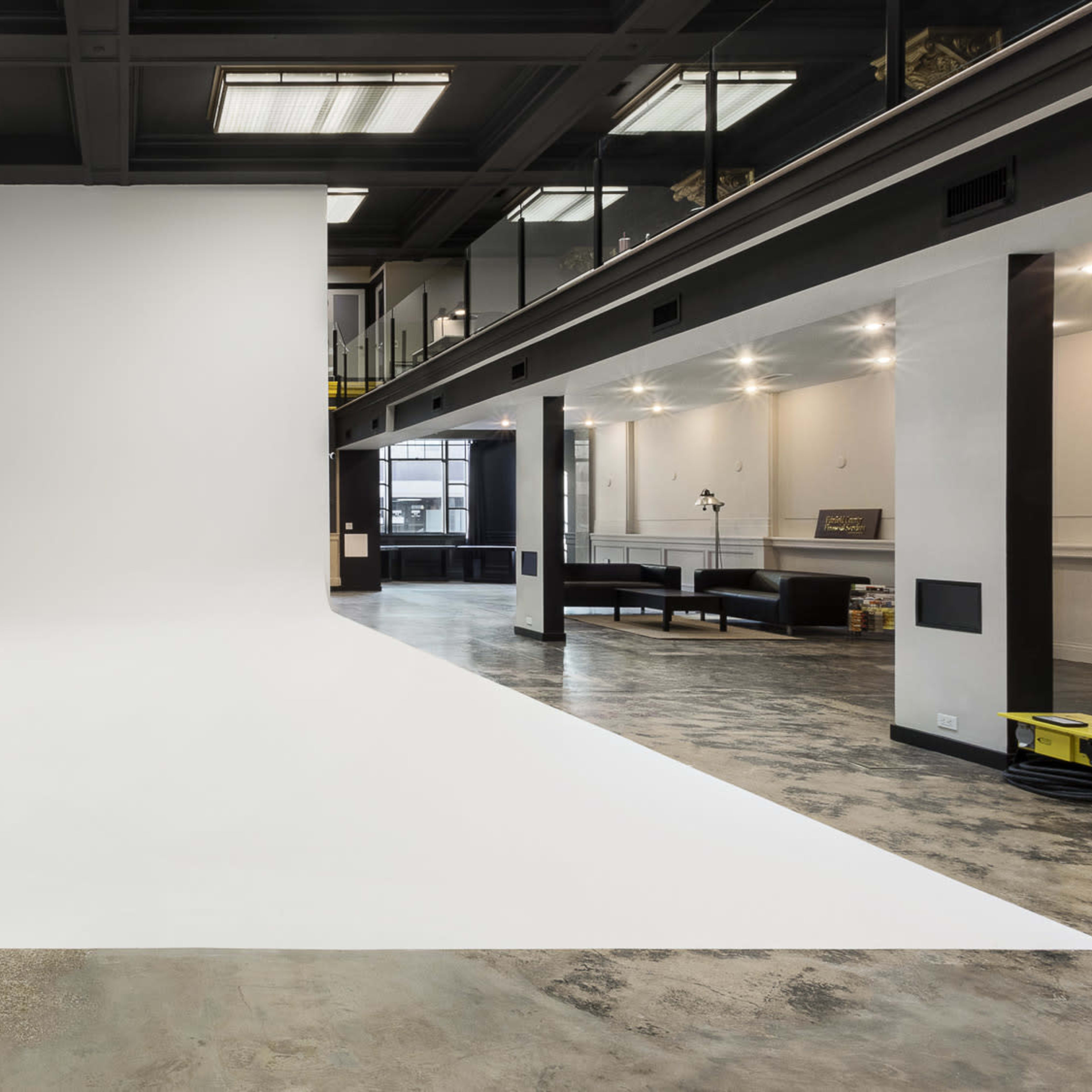 An empty studio space features a large white backdrop and a concrete floor, with a modern design and industrial lighting.
