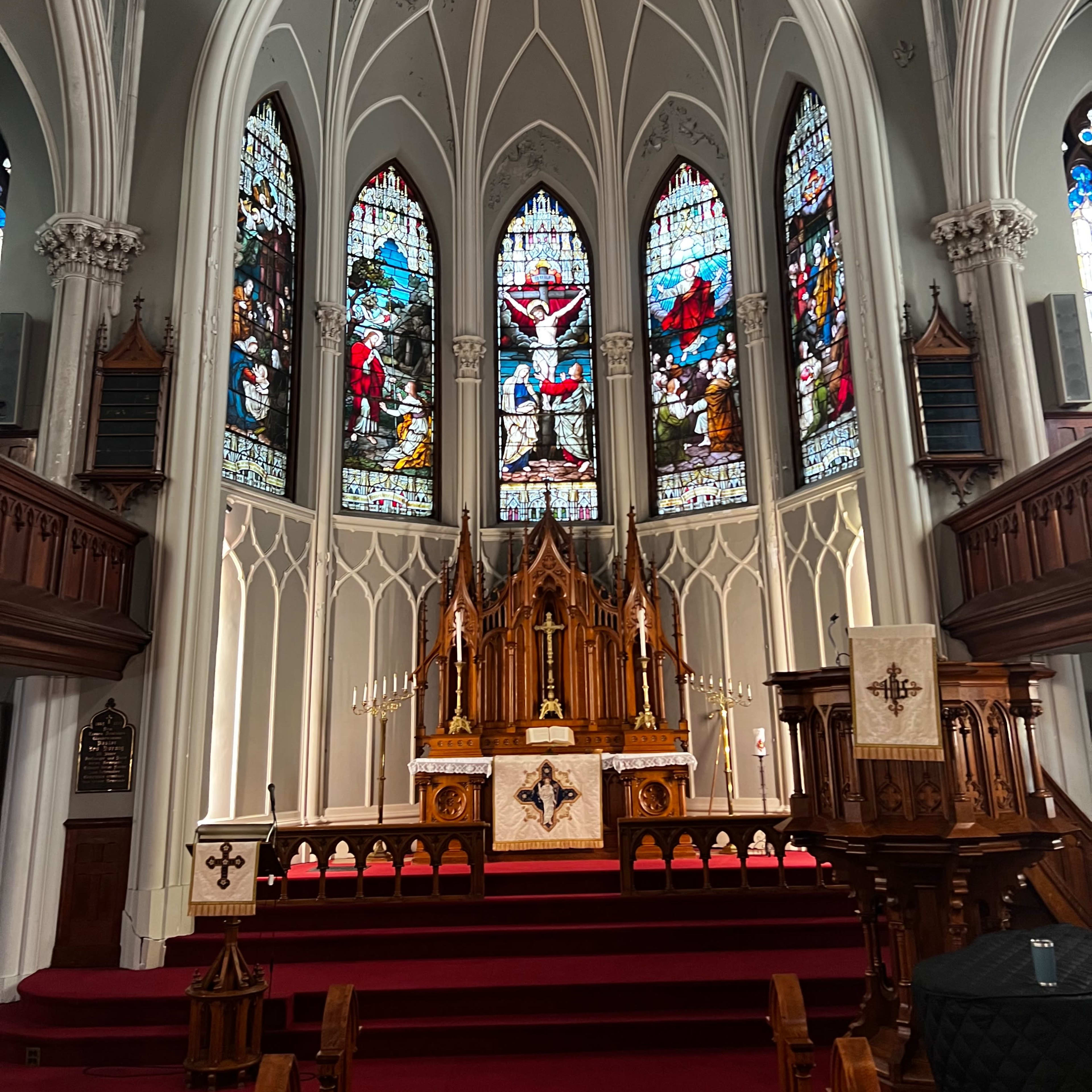 The interior of a church featuring an altar with elaborate woodwork and stained glass windows depicting biblical scenes.