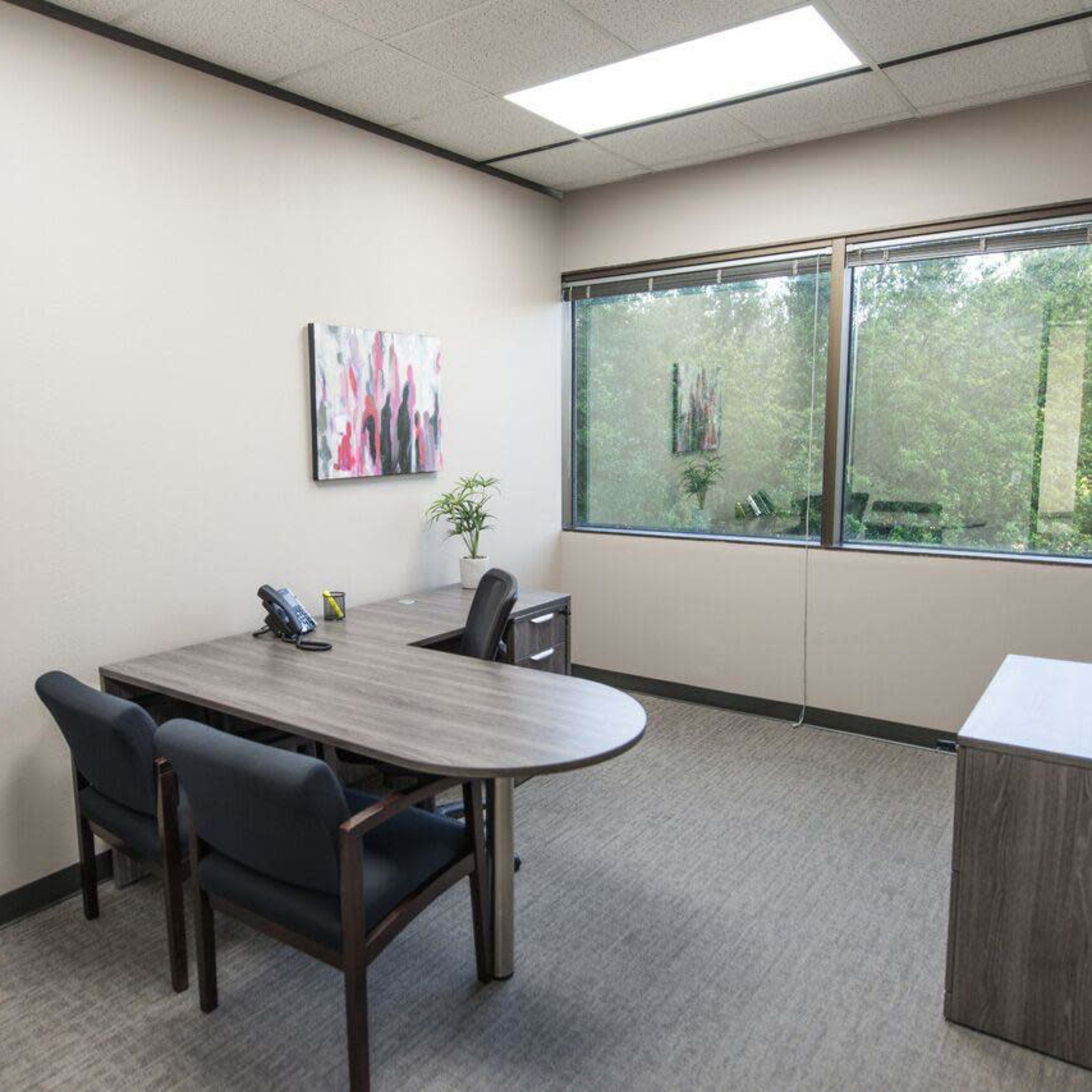 A small office with a round table, two chairs, a phone, and a window overlooking trees.