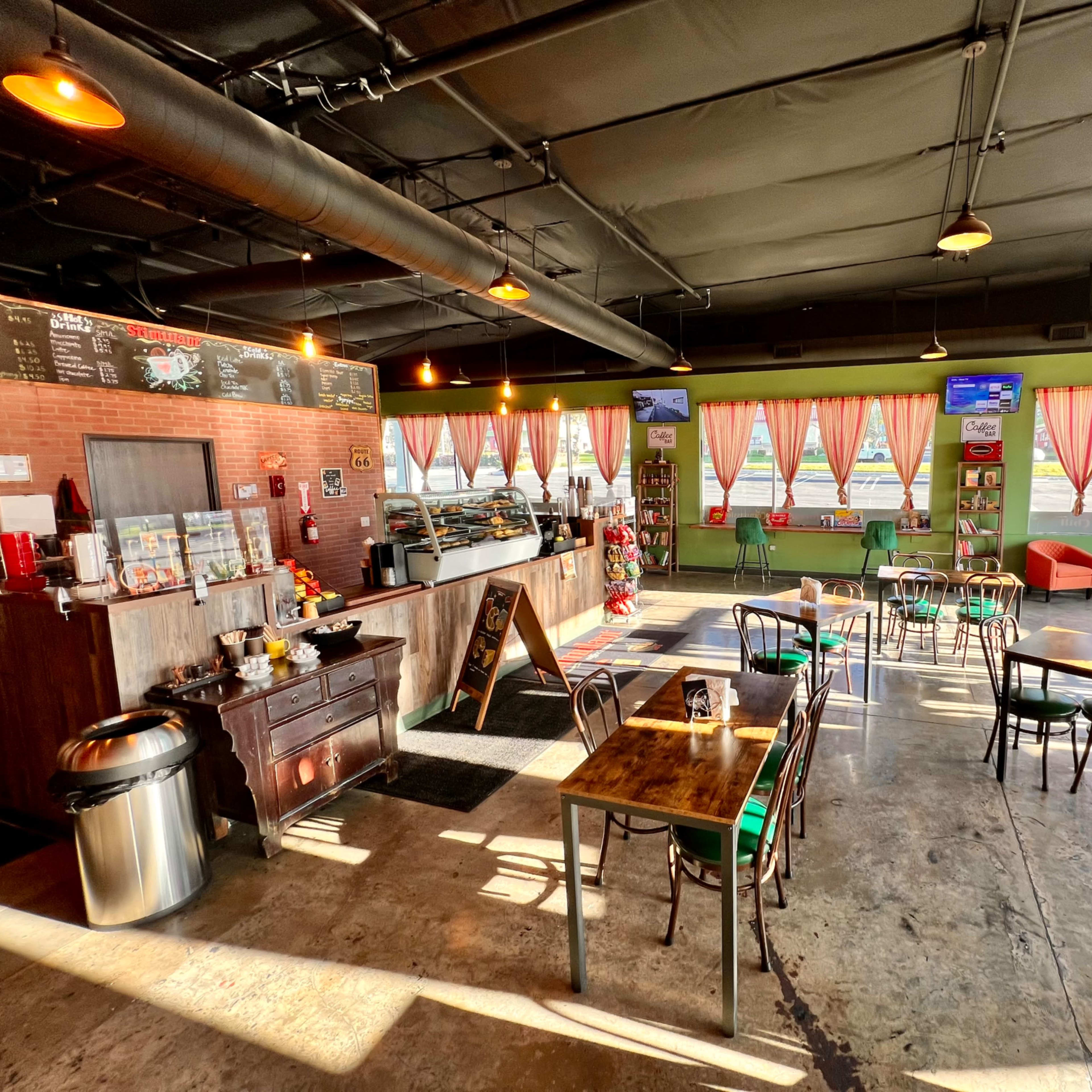 A spacious café with wooden tables, chairs, a service counter, and large windows adorned with curtains.