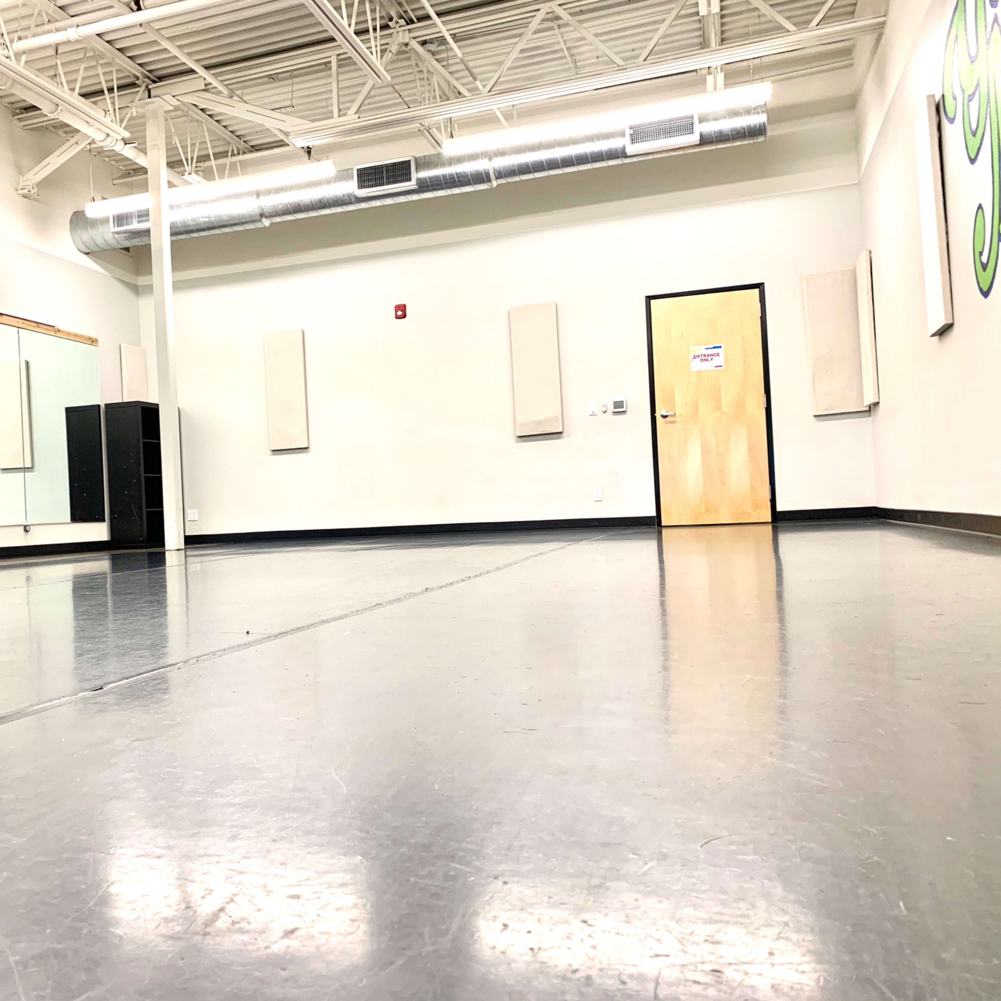 A spacious dance studio with a mirrored wall, wooden flooring, and muted decor.