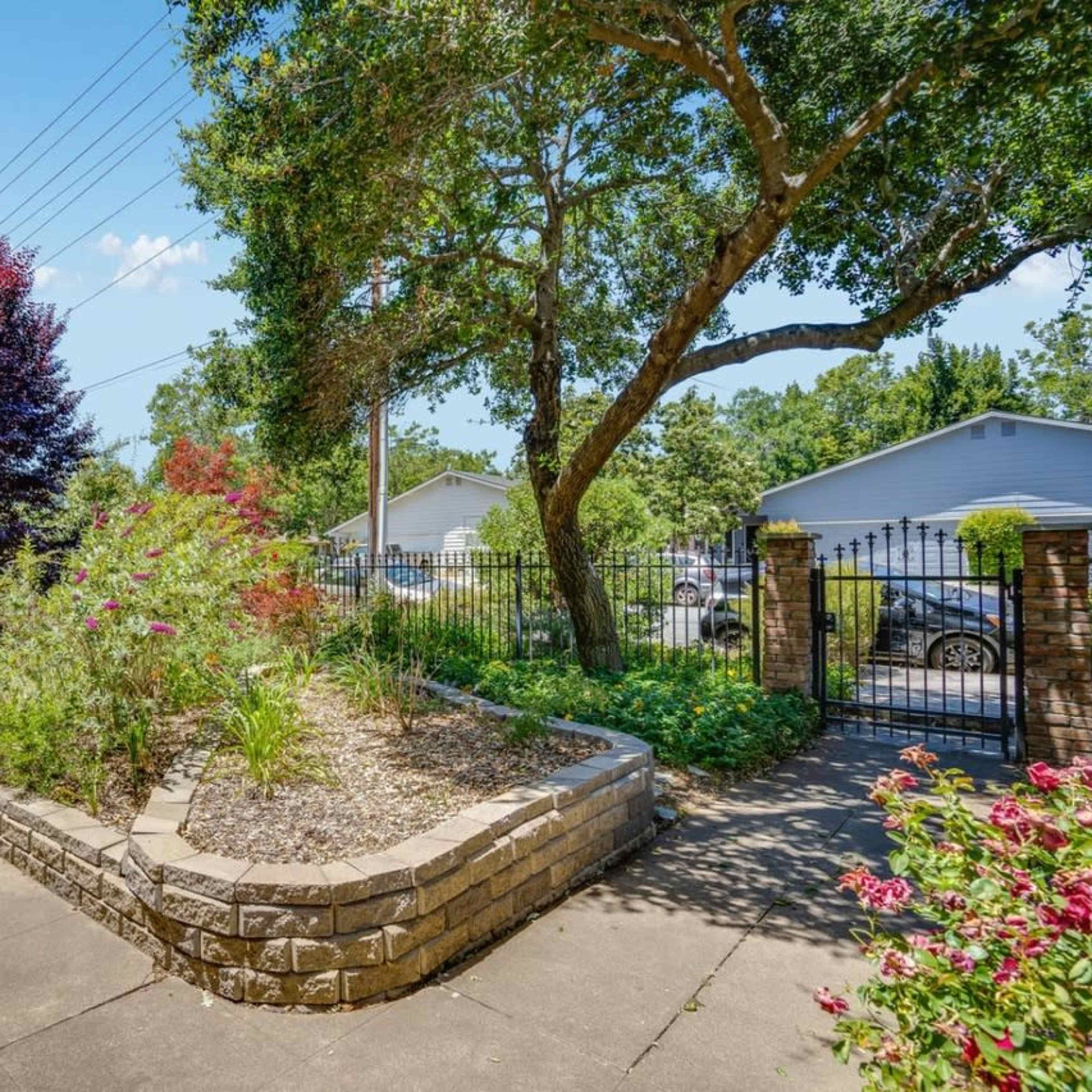 A landscaped path leads to a gated entrance, flanked by colorful shrubs and trees.