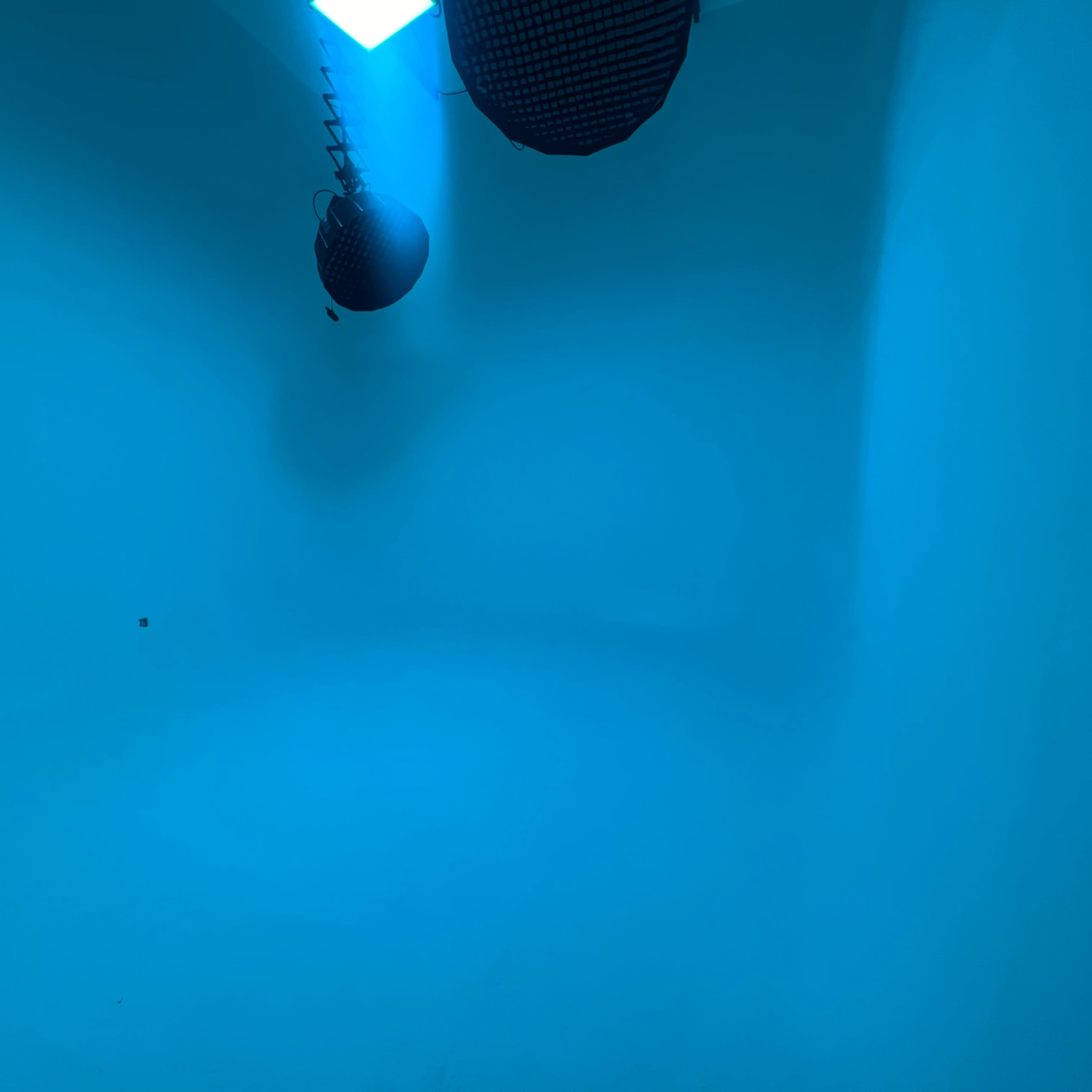 A room with blue walls and two hanging fixtures emitting blue light.