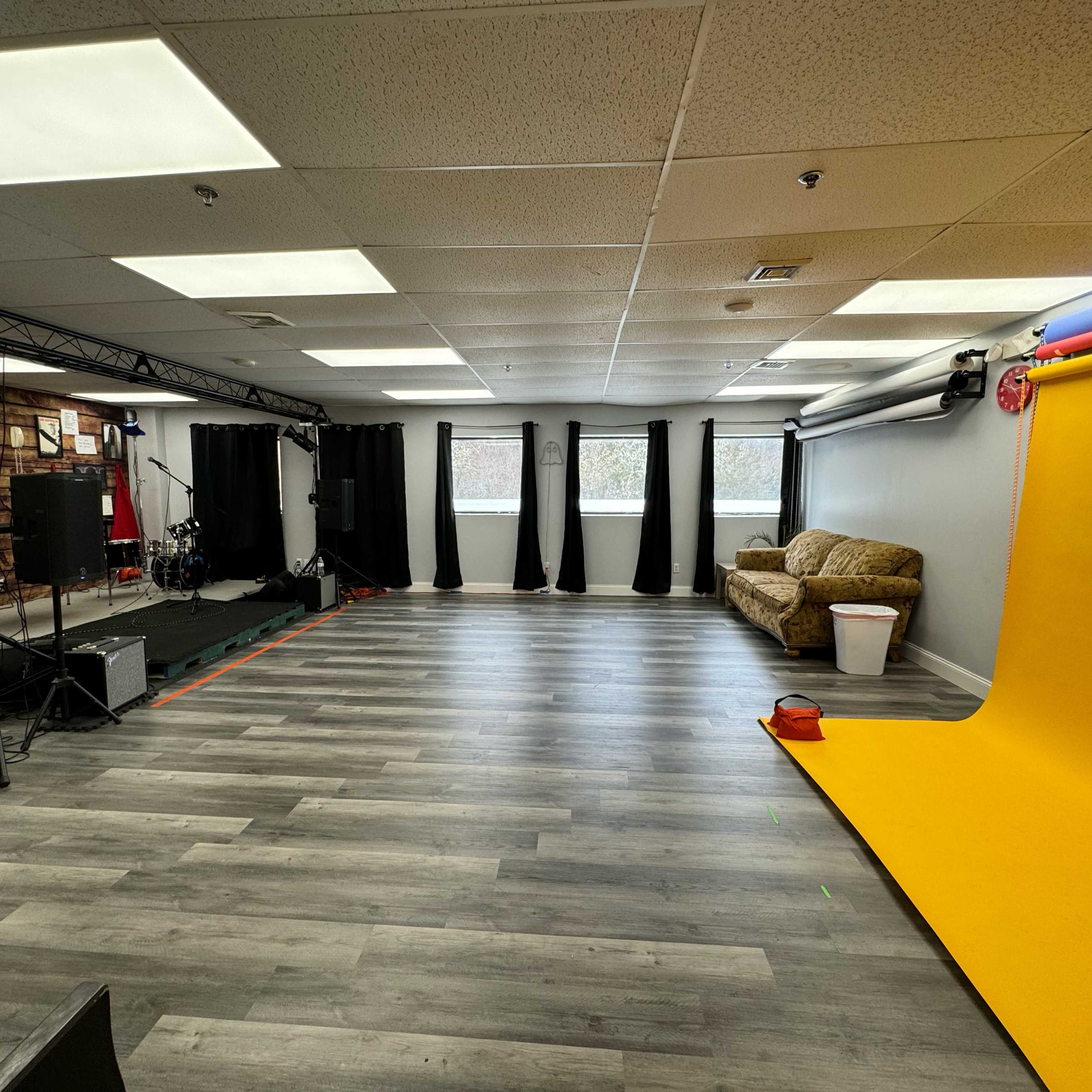 A spacious studio with a yellow backdrop, a couch, and various equipment set up for filming or photography.