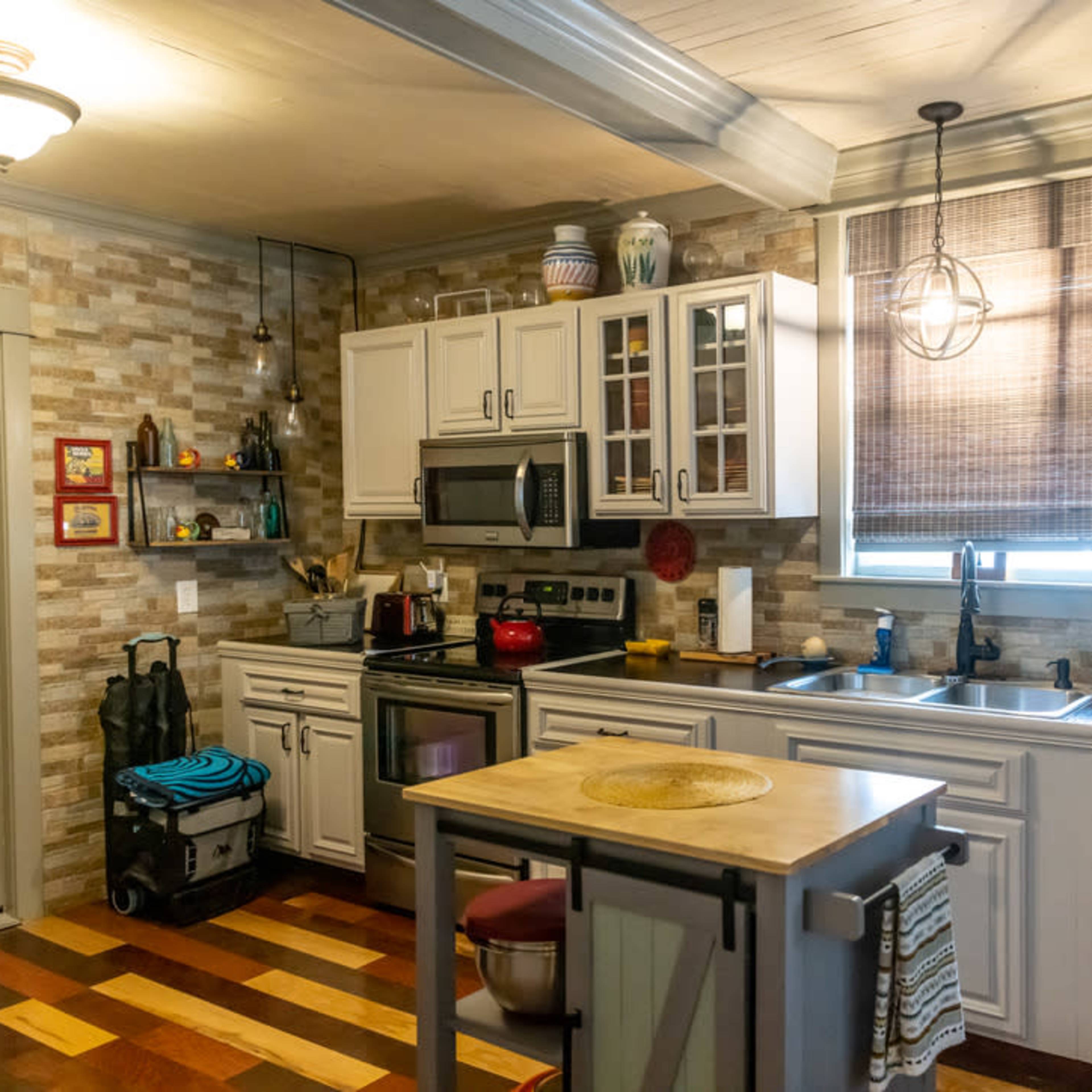 A modern kitchen with light-colored cabinets, a stainless steel sink, and a central island with a round top, set against a wall of textured stone.