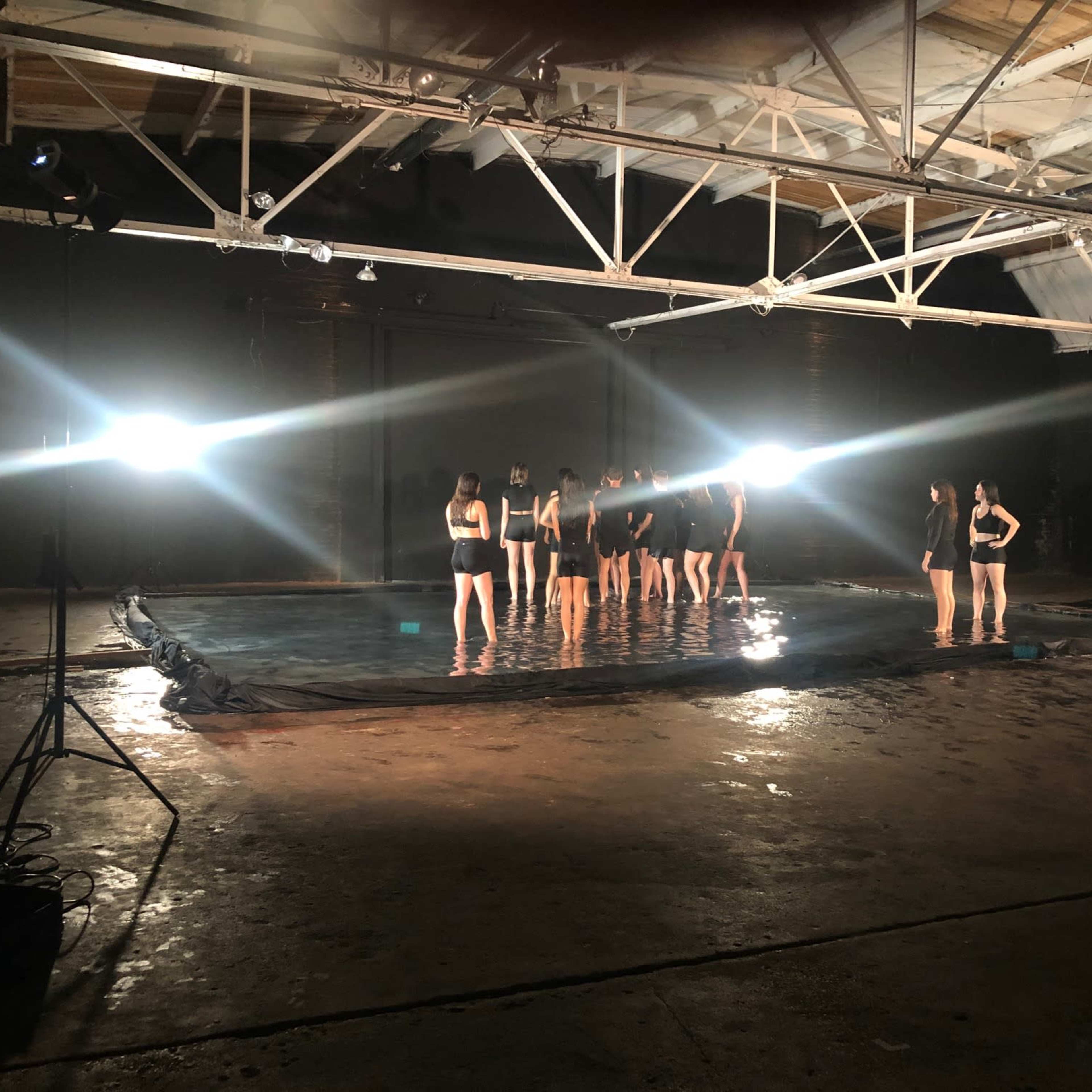 A group of individuals stands in a pool of water illuminated by bright lights in an industrial space.