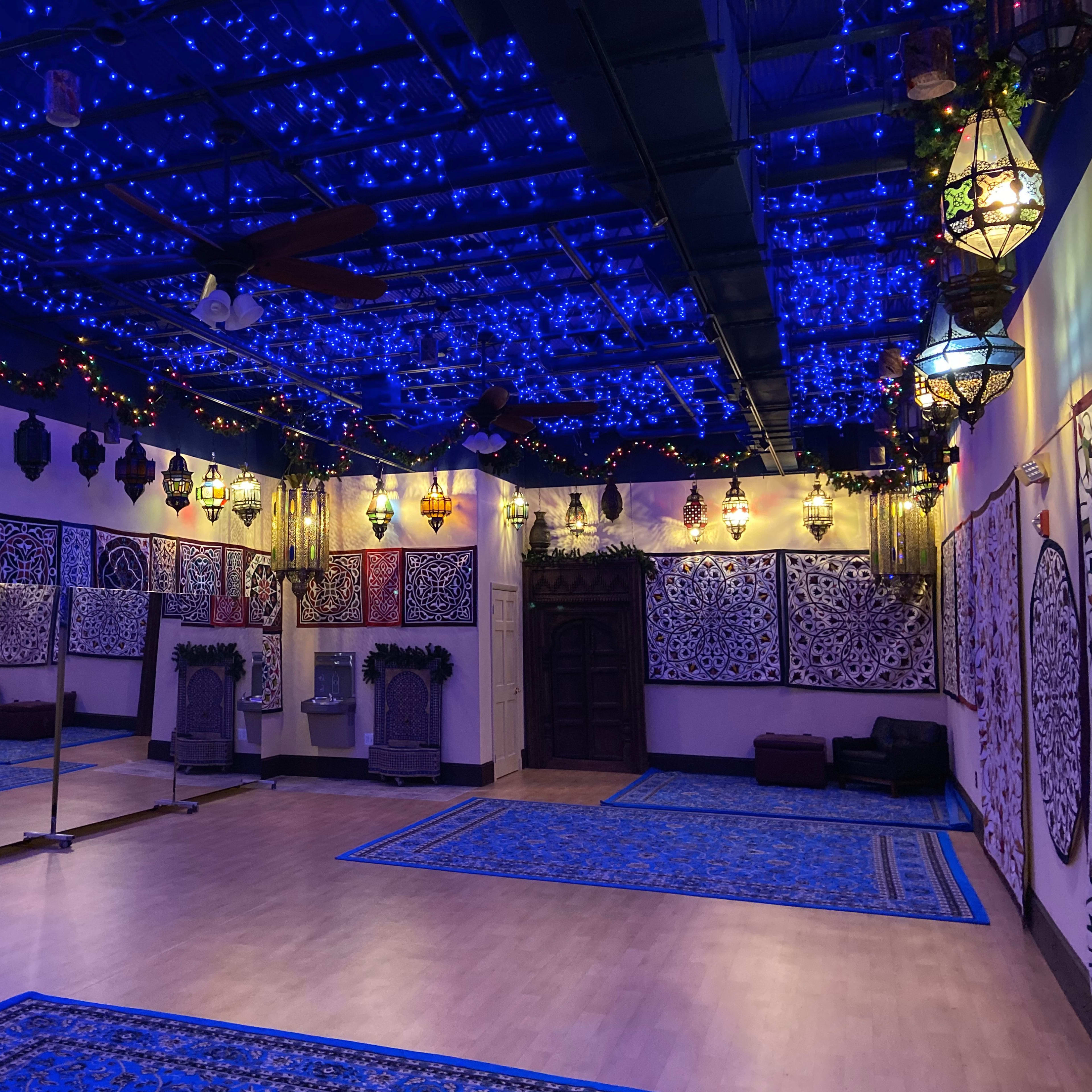The room features illuminated blue ceilings adorned with string lights and decorative lanterns, with mirrors along one wall and patterned carpets covering the floor.