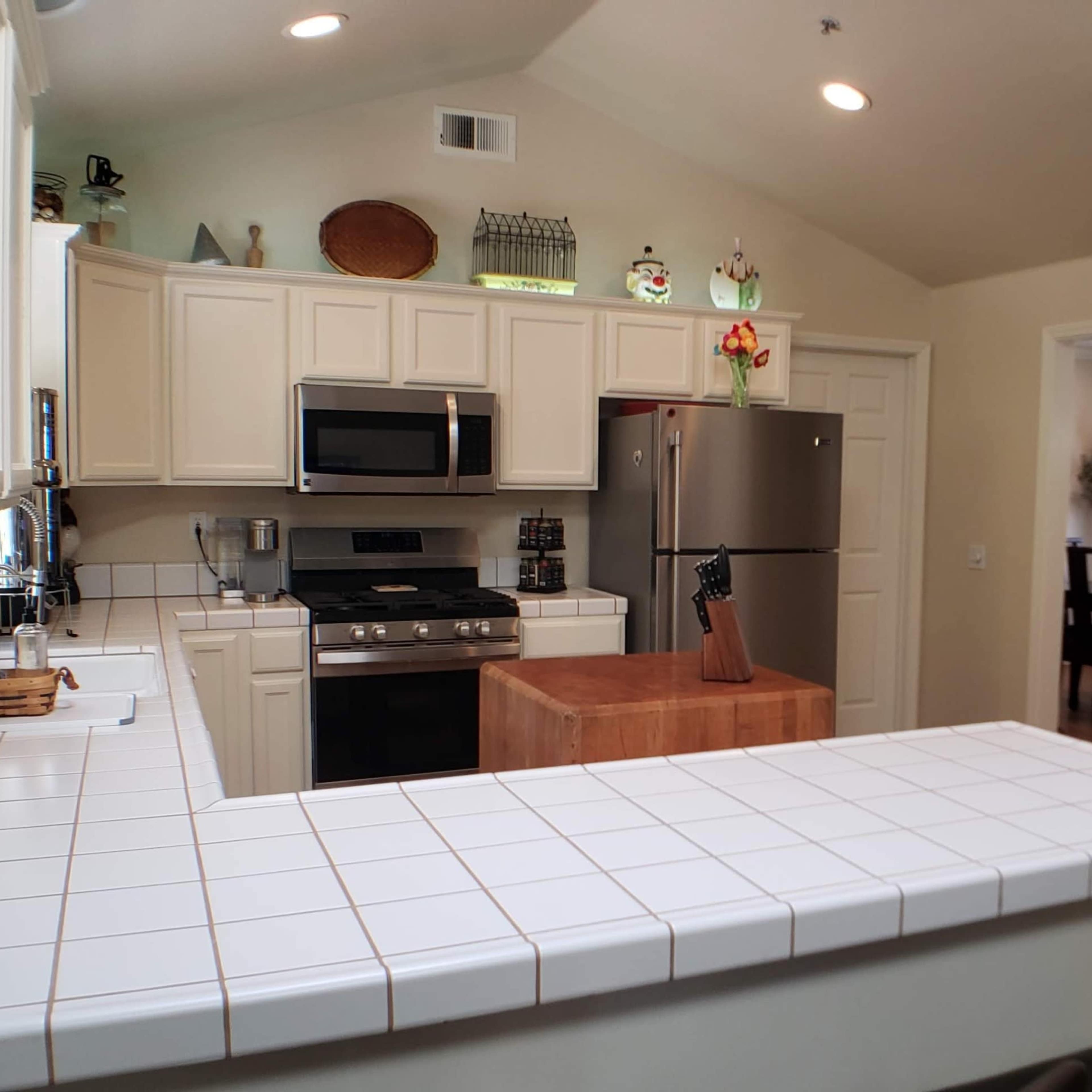 A modern kitchen with white cabinetry, stainless steel appliances, and a tile countertop separating it from a dining area.