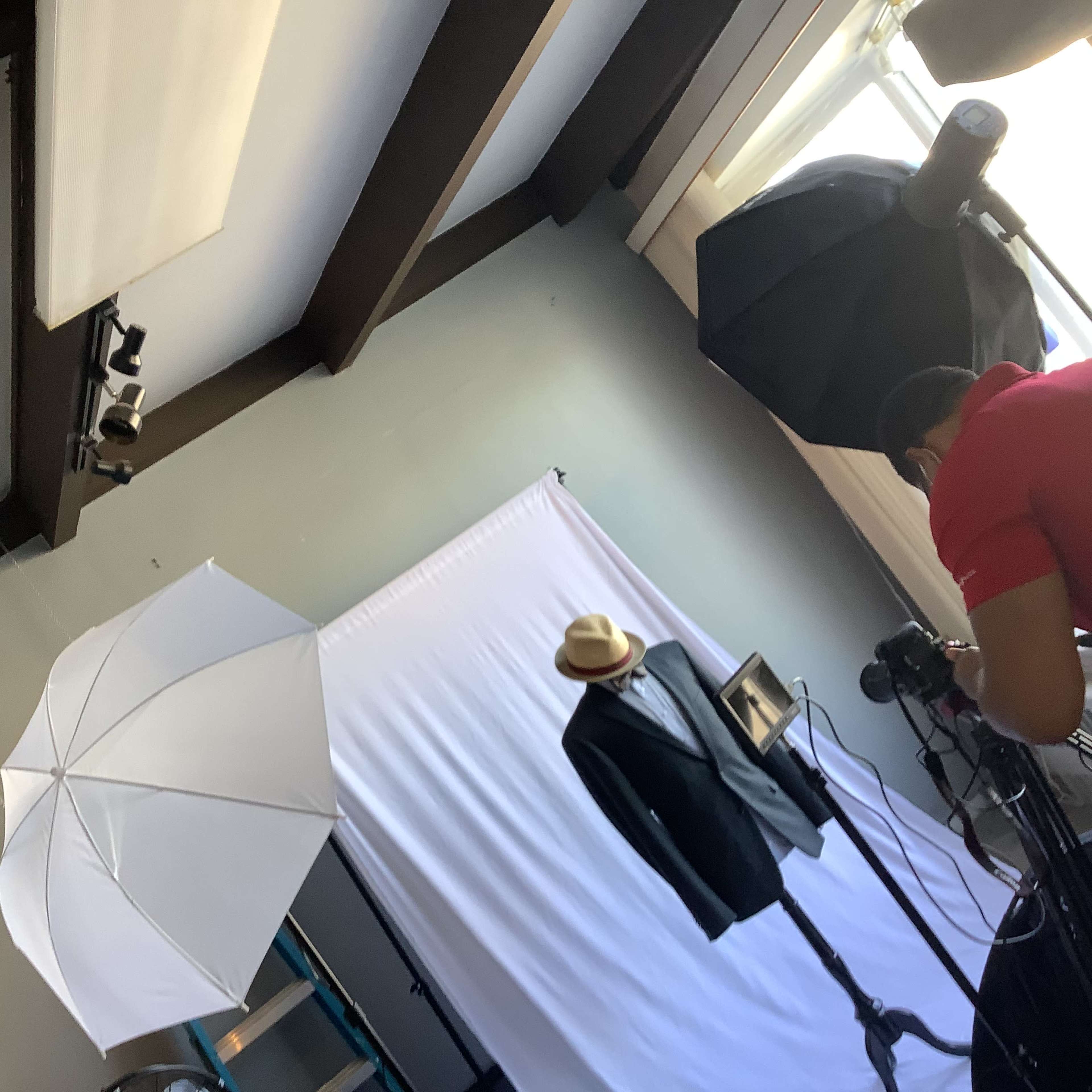 A photography setup featuring a suit on a mannequin, with a backdrop, lighting equipment, and a photographer adjusting the camera.