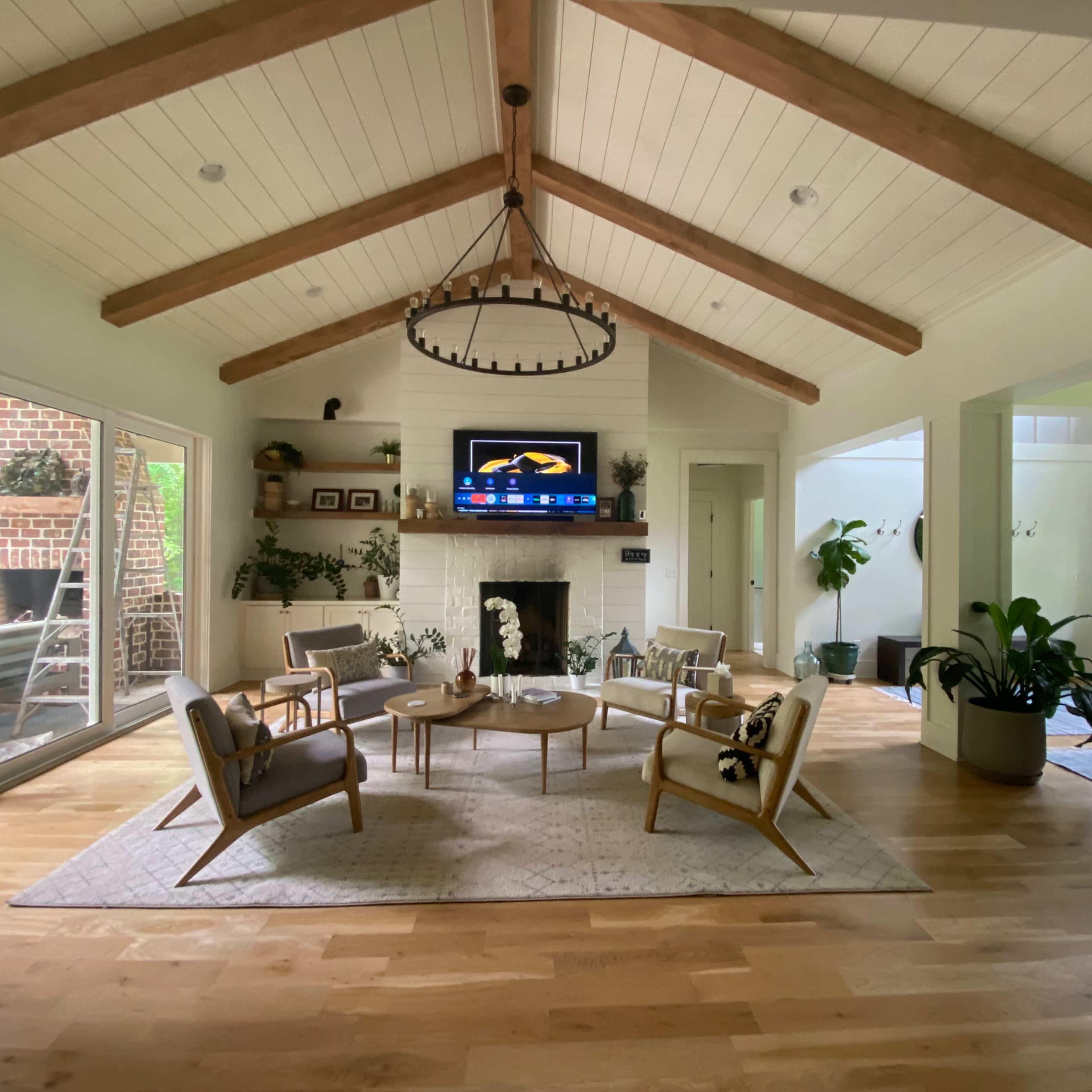 A spacious living room with a vaulted ceiling, wooden beams, a light-colored fireplace, and a seating arrangement centered around a coffee table.