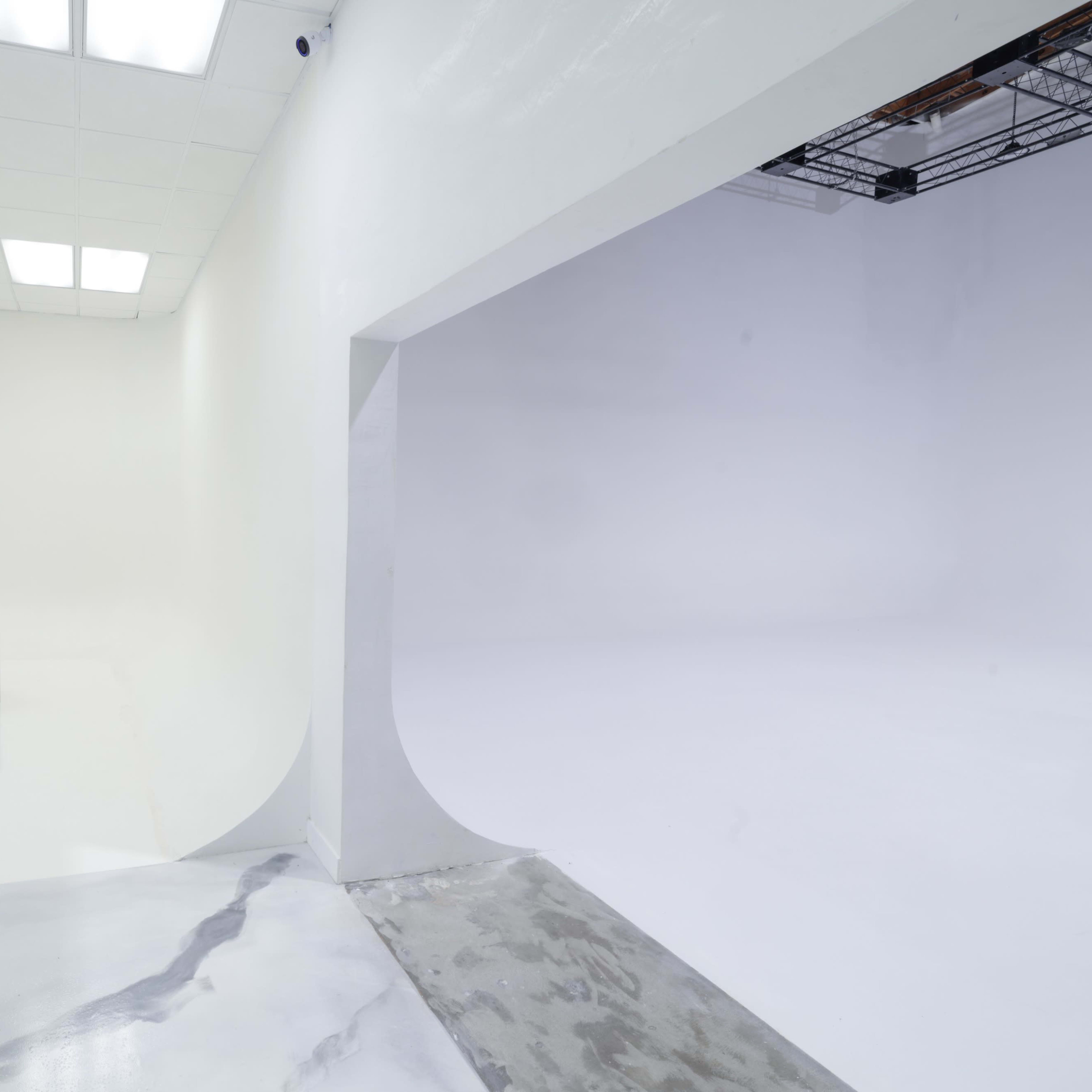 A spacious, well-lit studio with white walls and two distinct areas, one featuring three gray cubes on a smooth surface and the other an empty, completely white space.