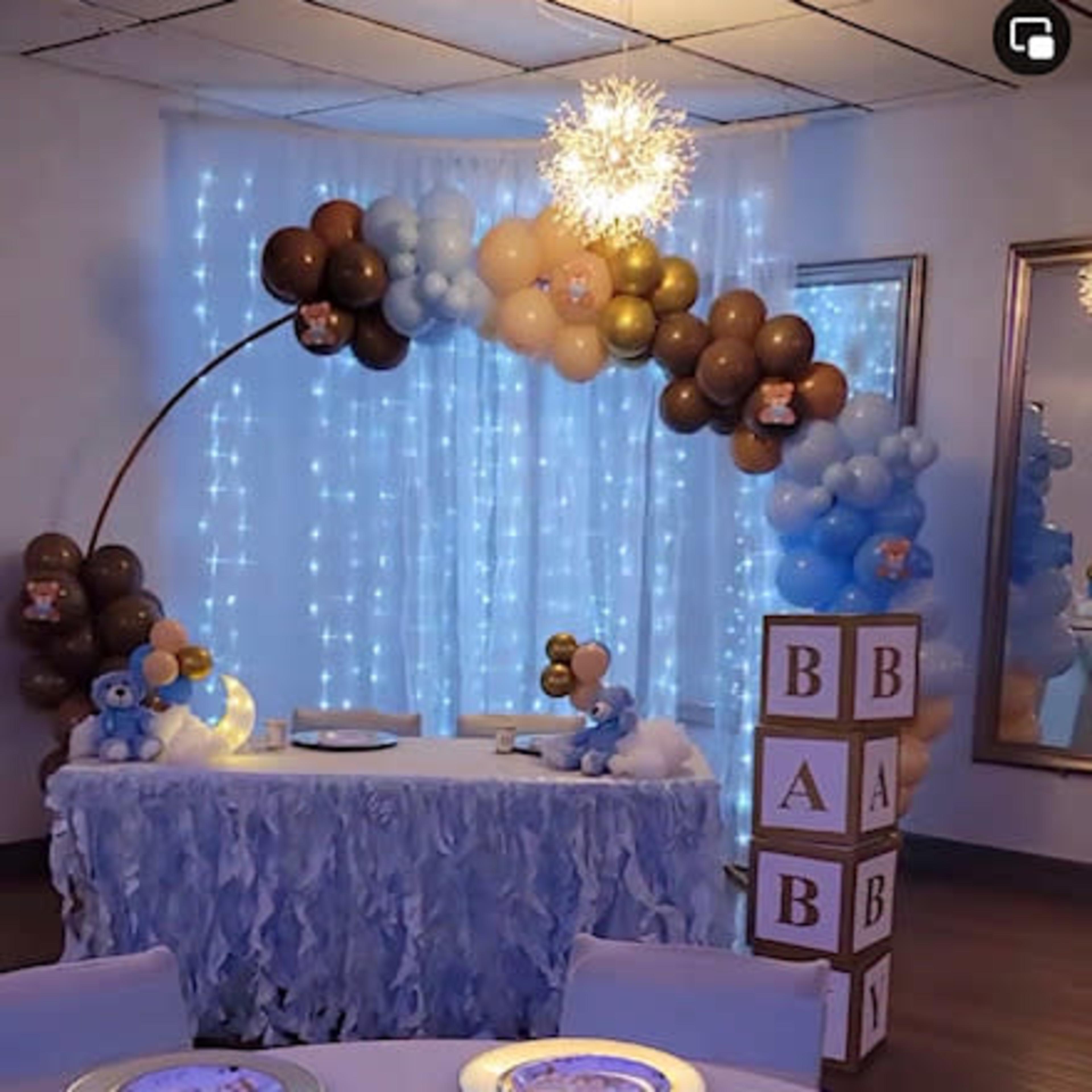 A decorated room for a baby shower, featuring a balloon arch, a dessert table with a ruffled tablecloth, and themed table settings with a teddy bear centerpiece.