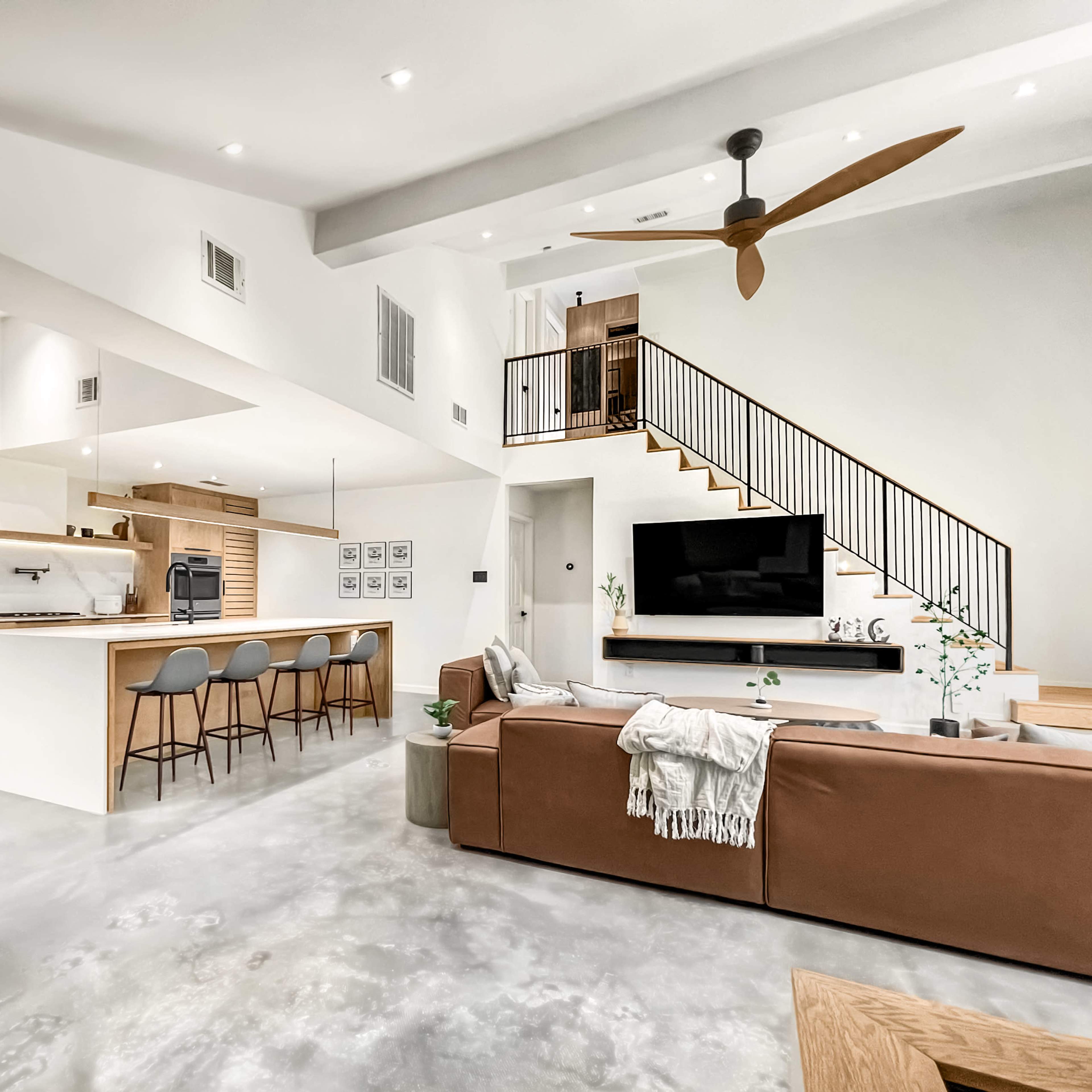 A modern open-concept living space featuring a kitchen, dining area, and a living room with a staircase leading to an upper level.