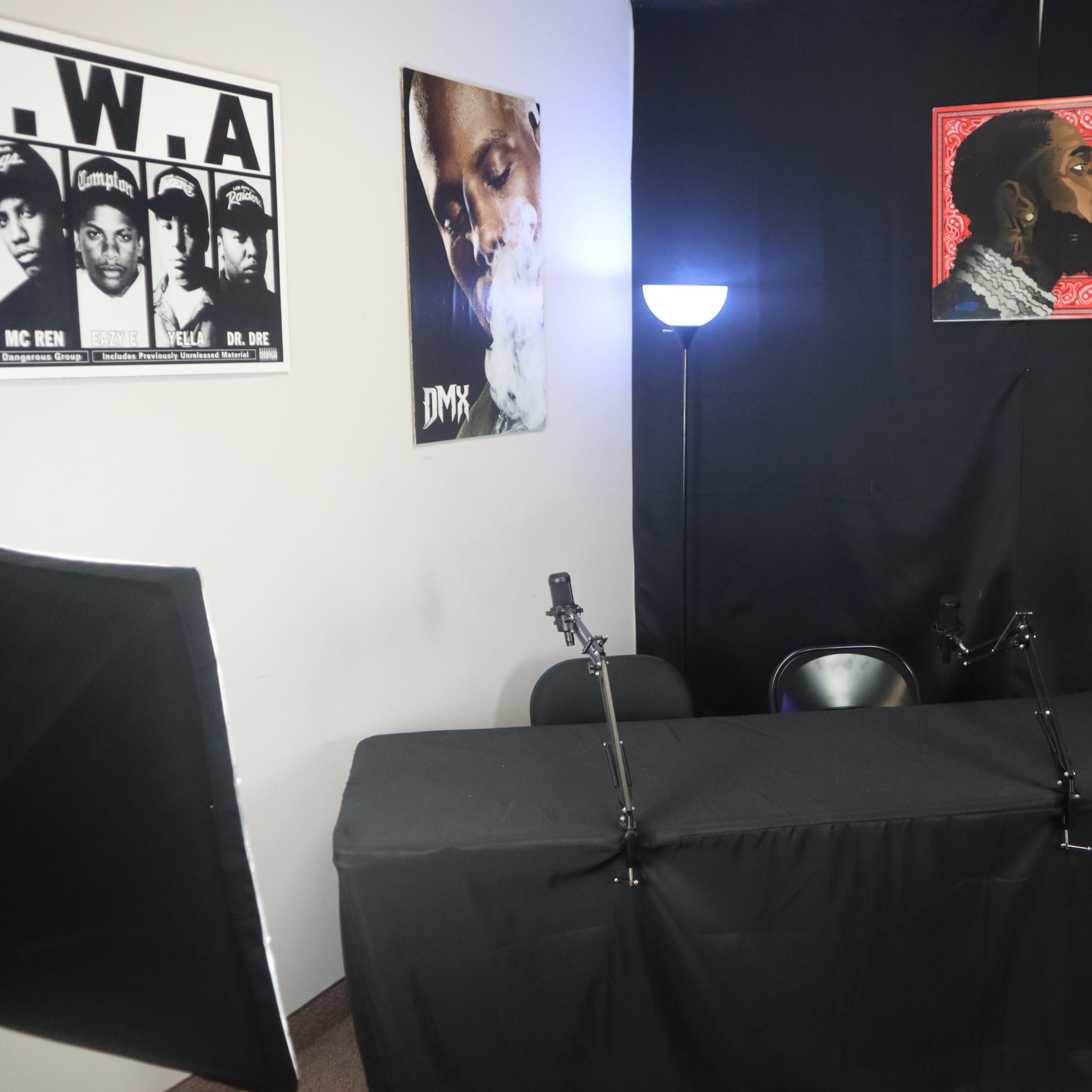 A small recording studio setup with a table covered in a black cloth, two microphones on stands, and posters of DMX and N.W.A on the walls.