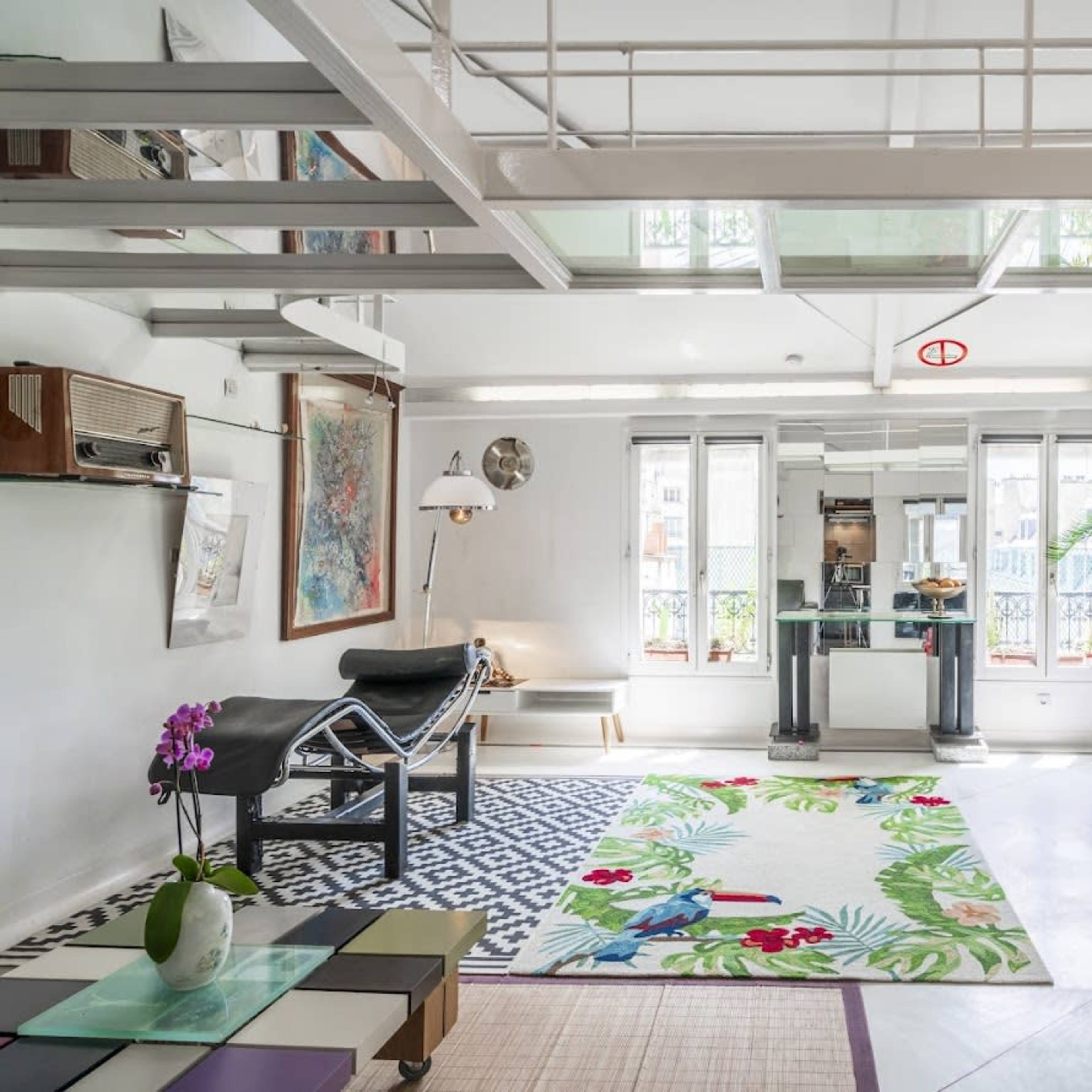 A bright, modern living space with a mix of furniture, including red chairs, a chaise lounge, and various artwork on the walls.
