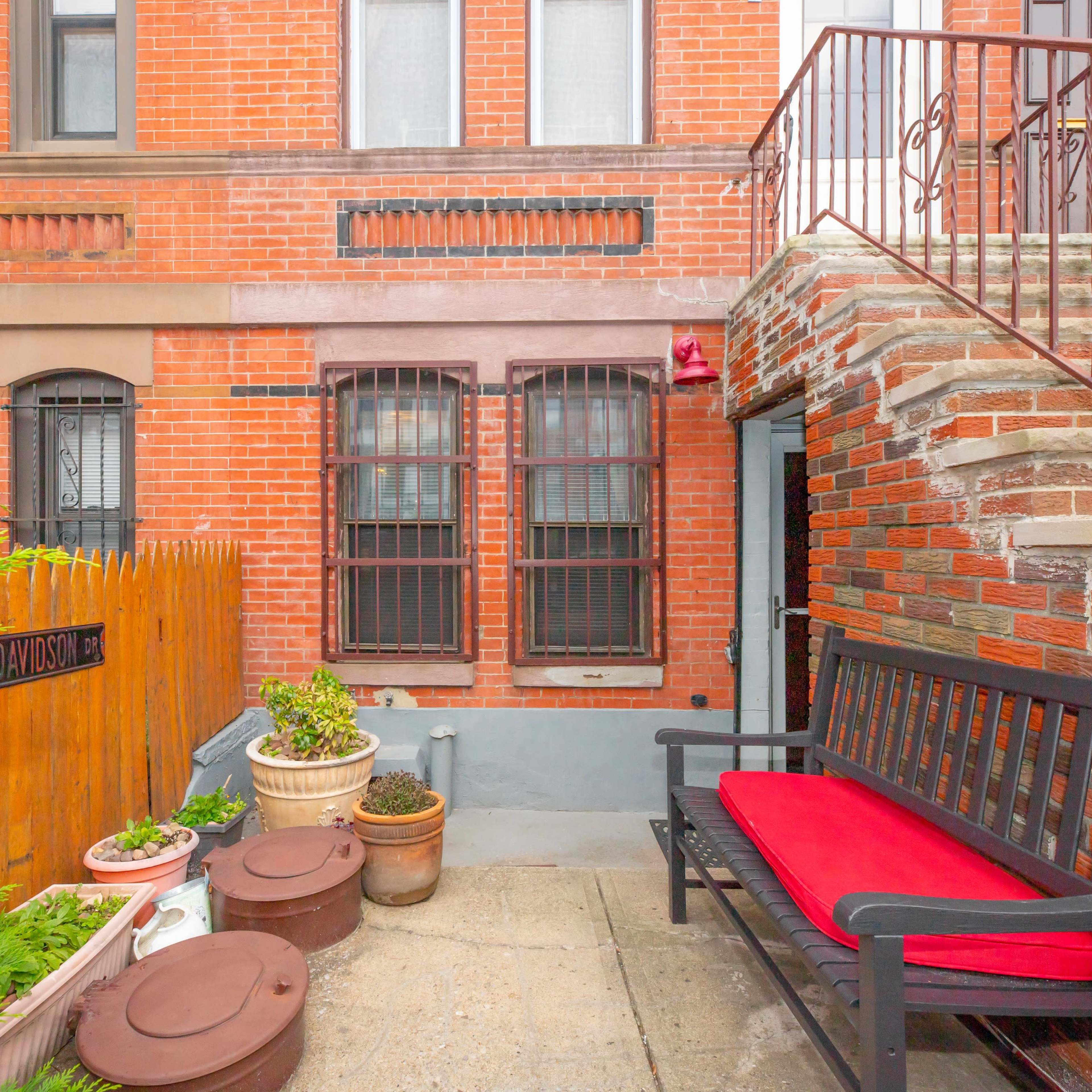 A brick courtyard with a bench, decorative planters, and a set of stairs leading to an upper level.