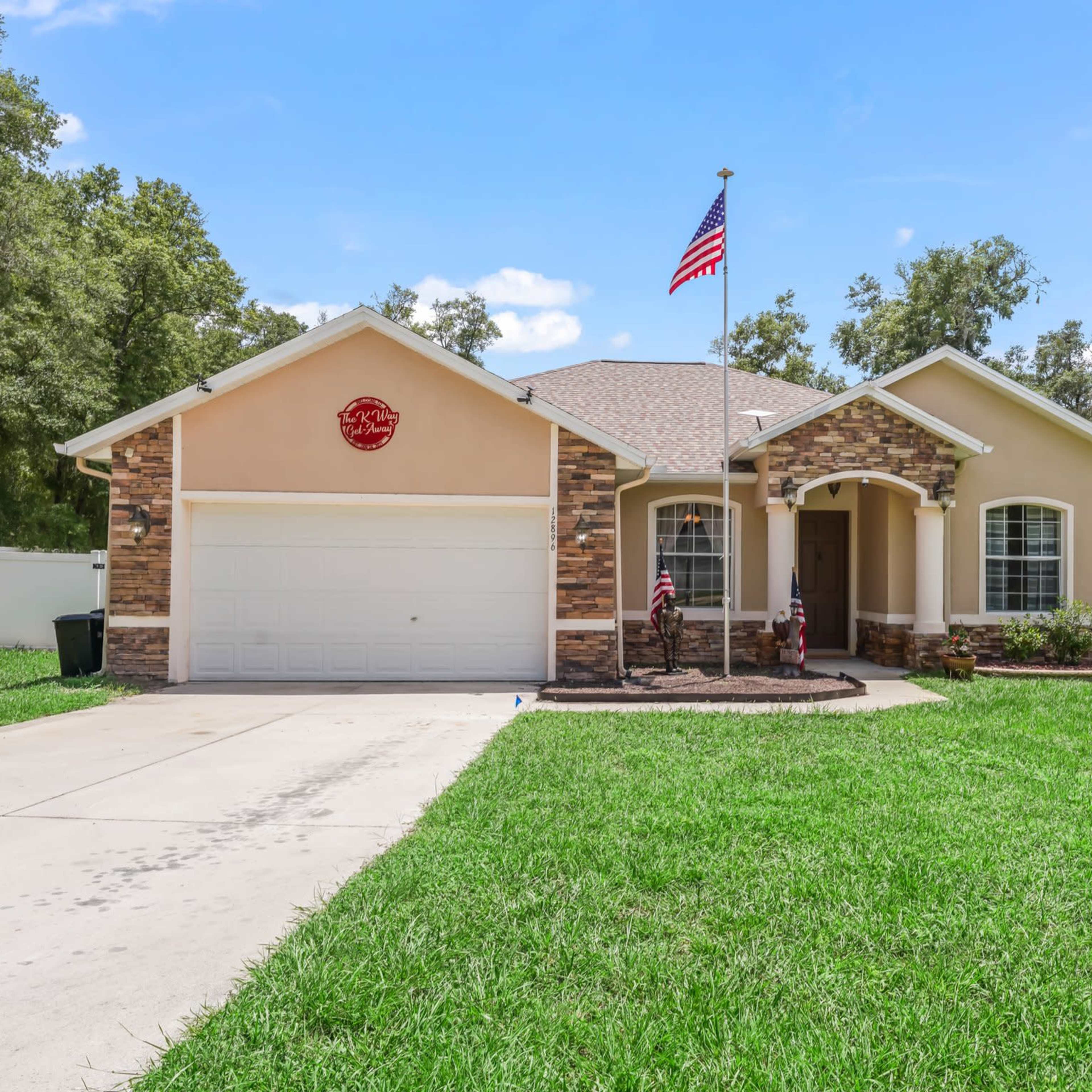 A single-story home features a stone accent facade, a front porch, an American flag, and a neatly manicured lawn.