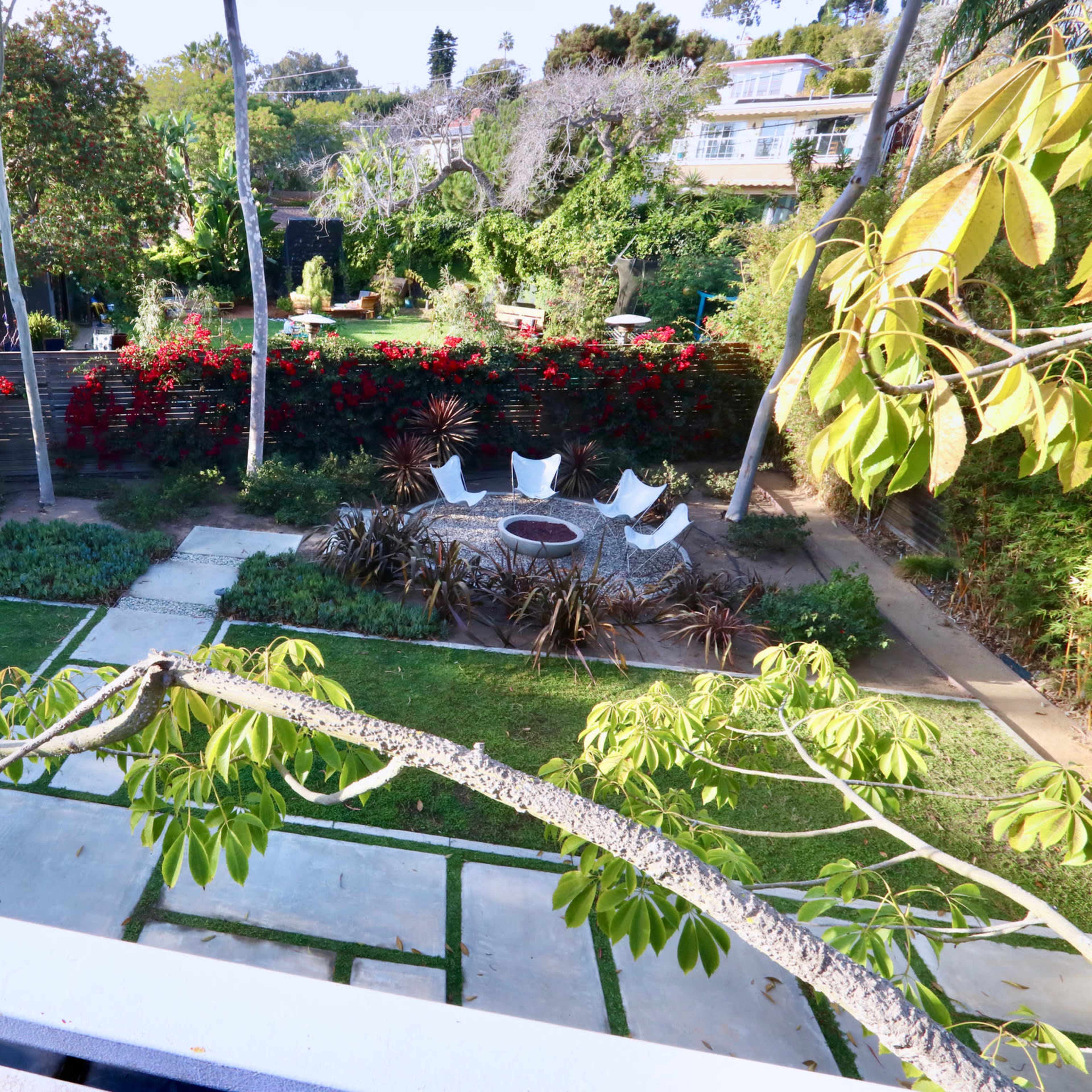 A landscaped garden with a circular seating area surrounded by plants and pathways leading through lush greenery.