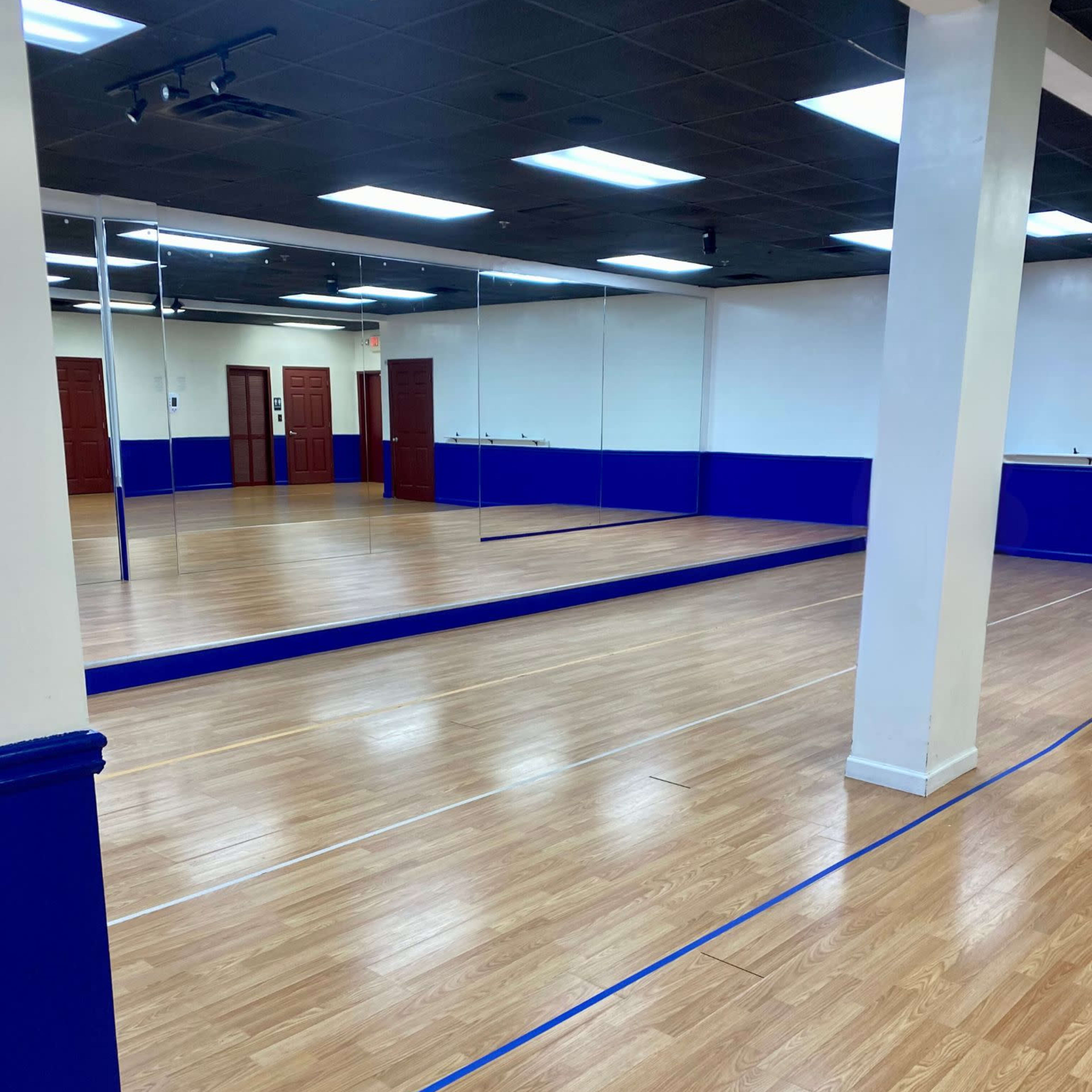 A spacious dance studio with a polished wooden floor, blue wall accents, and mirrored walls.