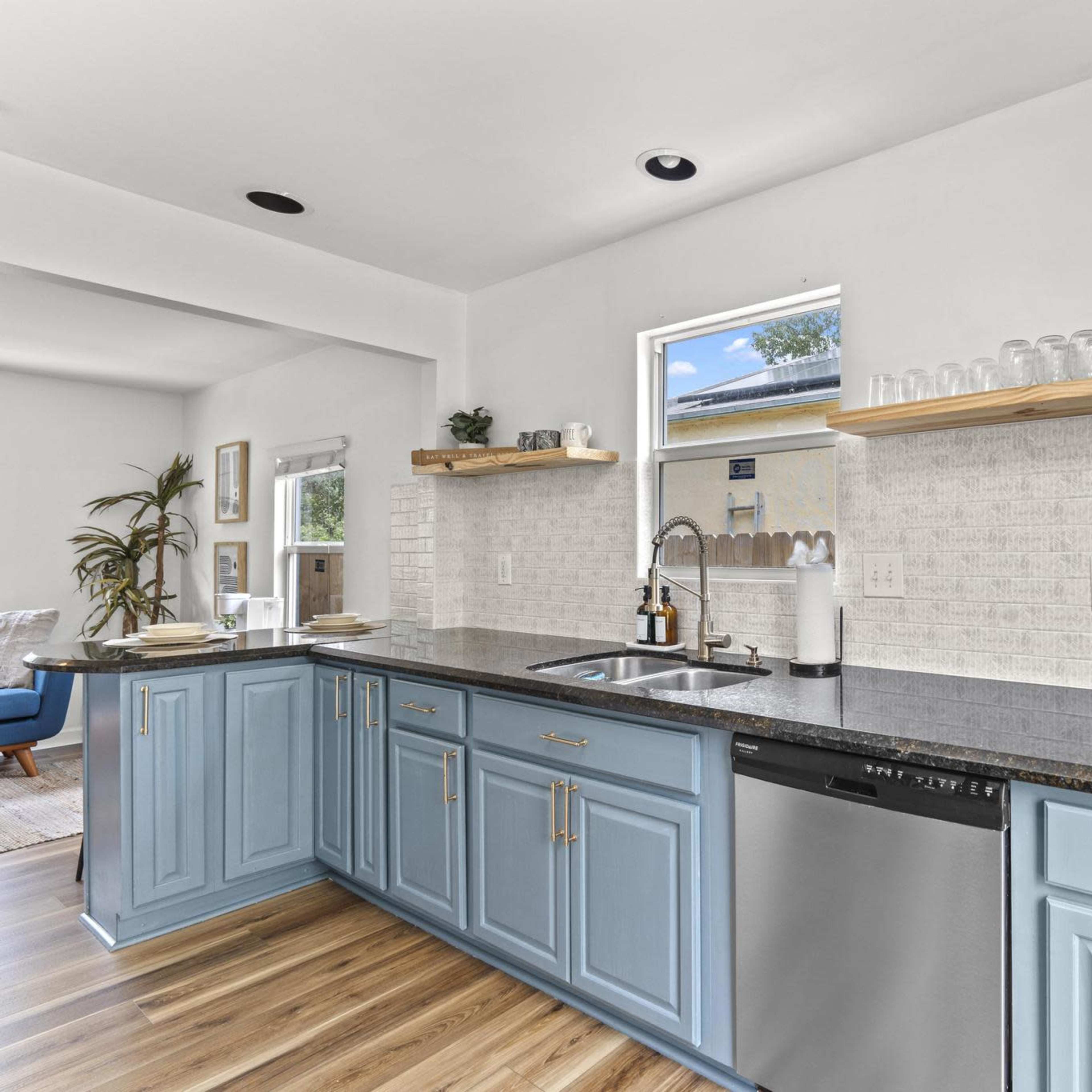 A modern kitchen features blue cabinets, a stainless steel sink, and open shelving with decorative items against a light-colored wall.