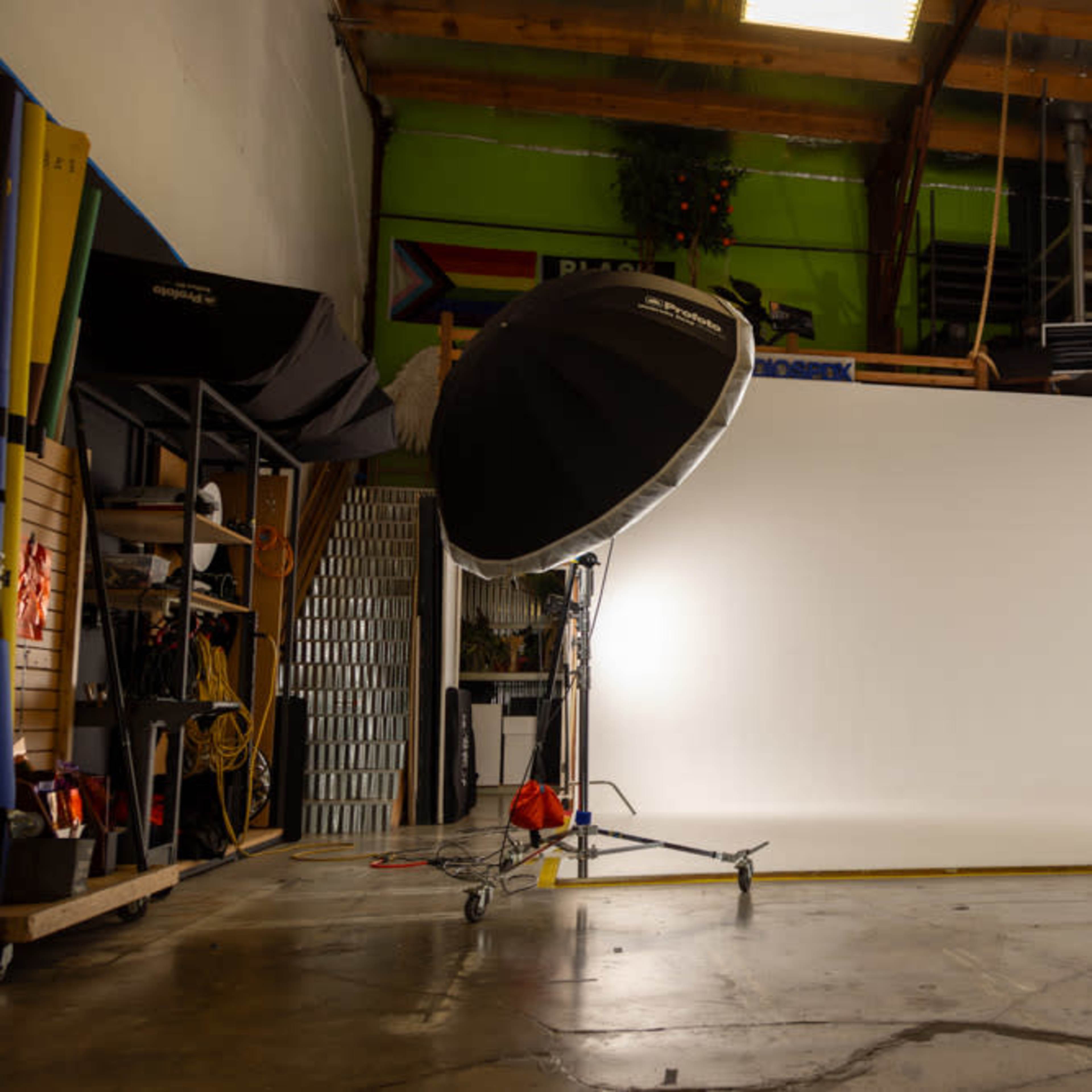 A photography studio featuring a white backdrop, lighting equipment, and various tools organized along the walls.