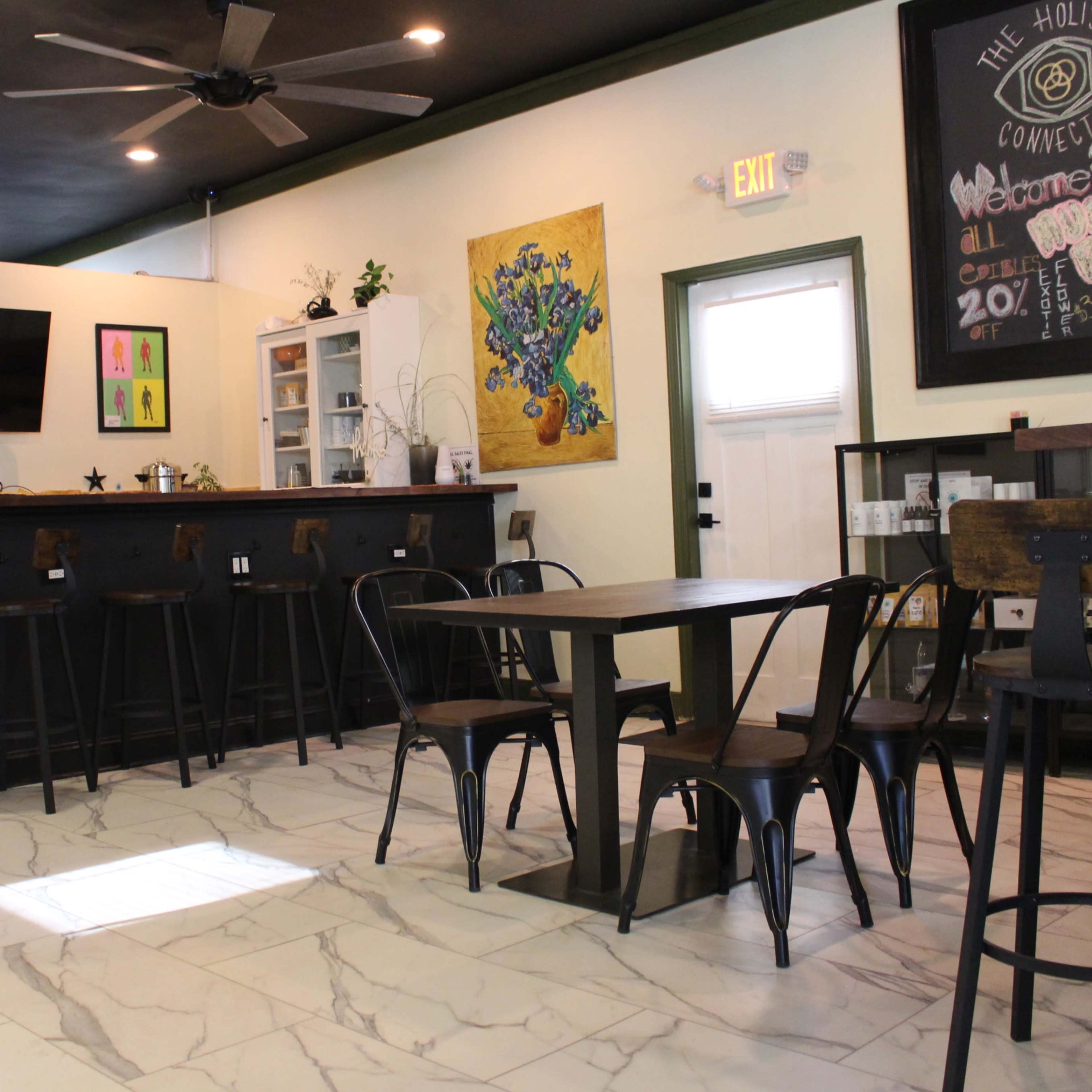 A cozy café interior with a bar counter, several tables, and colorful artwork on the walls.