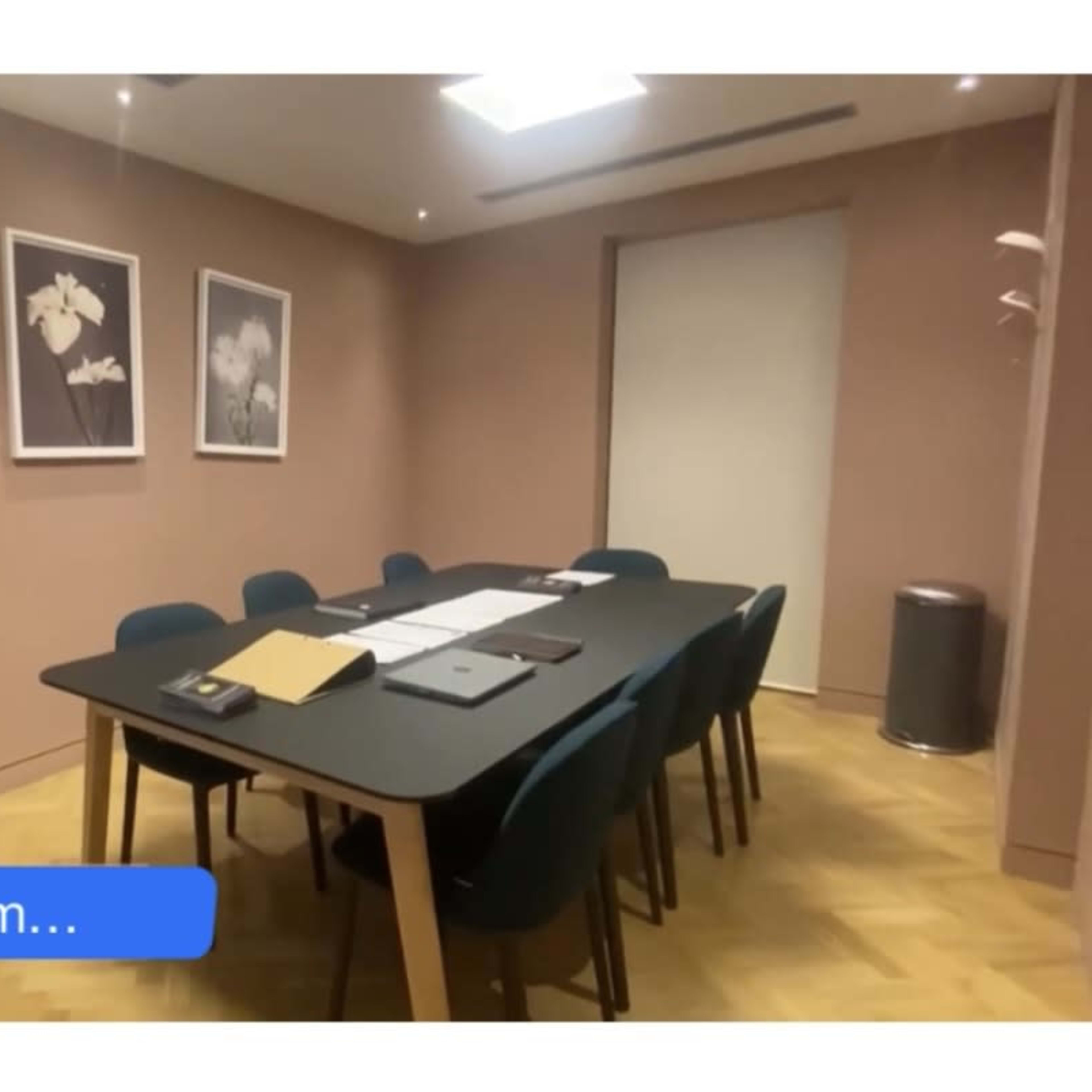 A private meeting room features a large table surrounded by chairs, with framed floral artwork on the walls.