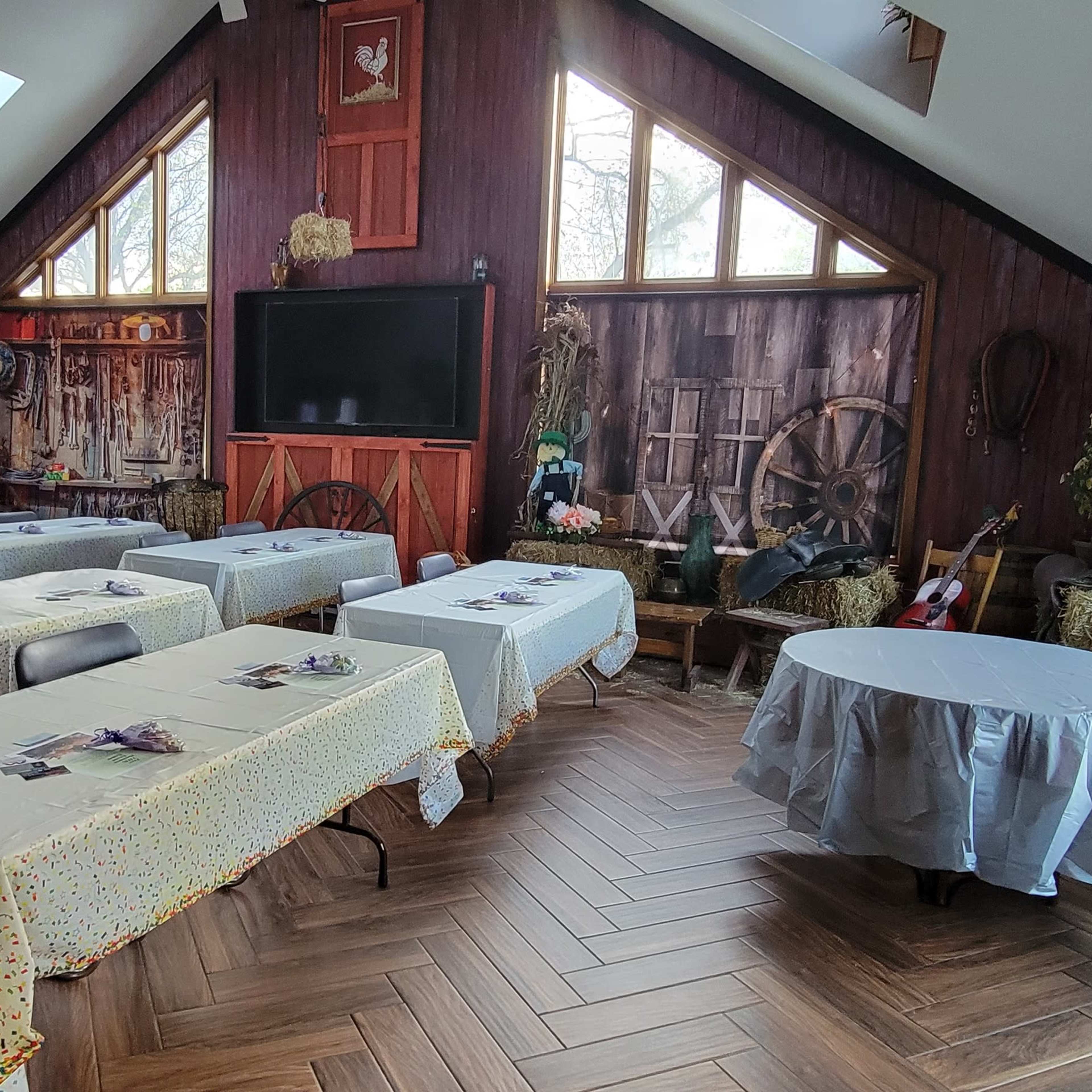 The room features several tables covered with white tablecloths, arranged in a spacious area with a large window and wooden decor.